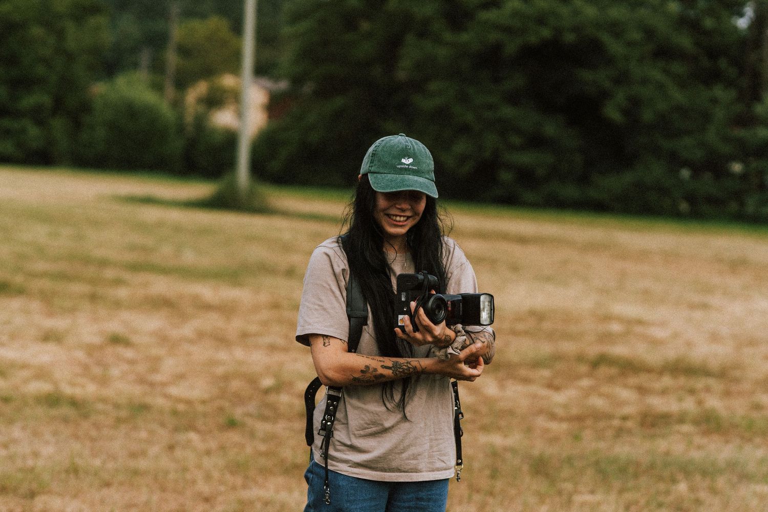 Photographer wearing a green baseball cap holds a vintage camera outdoors.