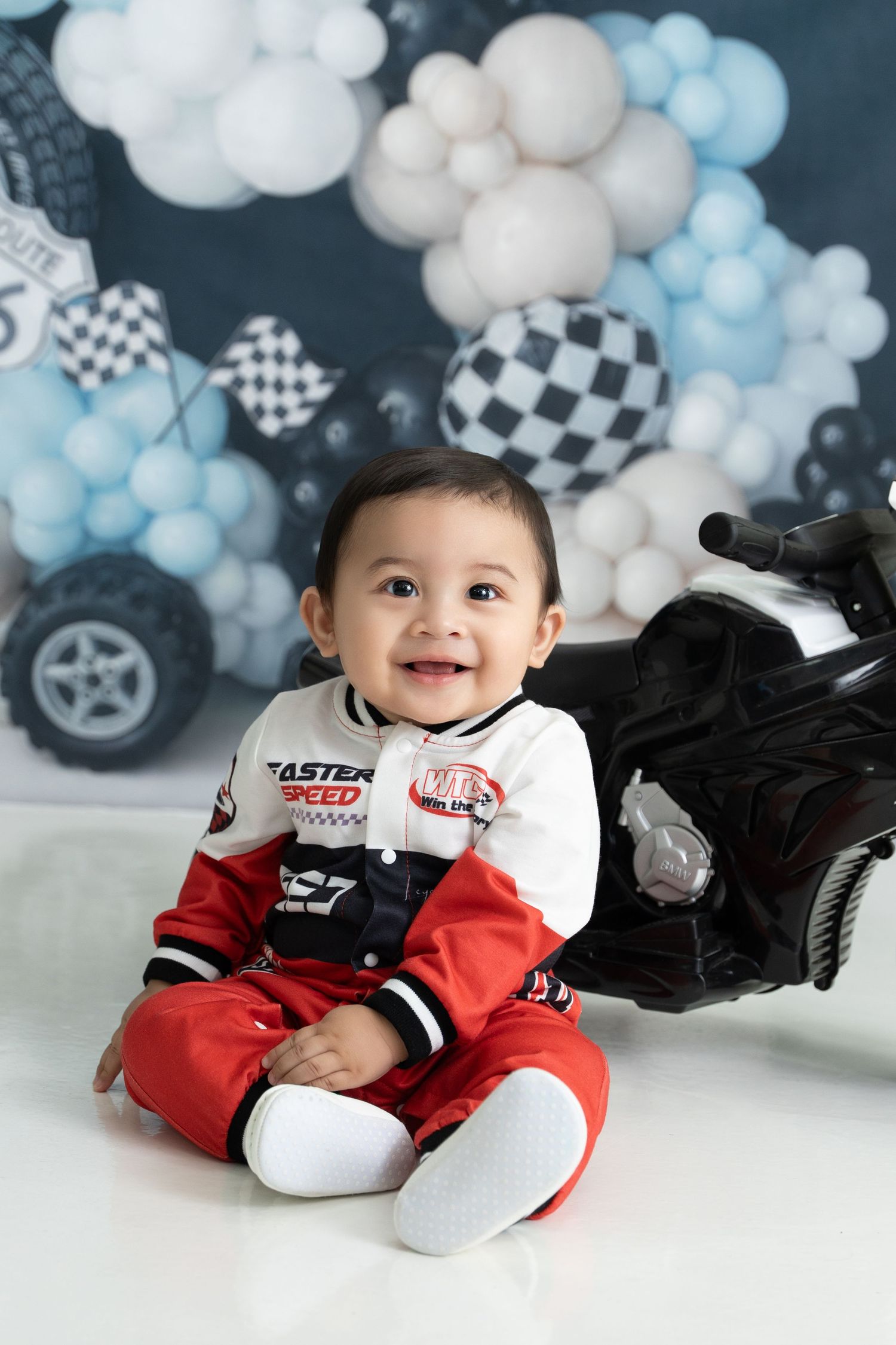 Racing themed baby photo session with blue and white balloon decorations and checkered flag accents.