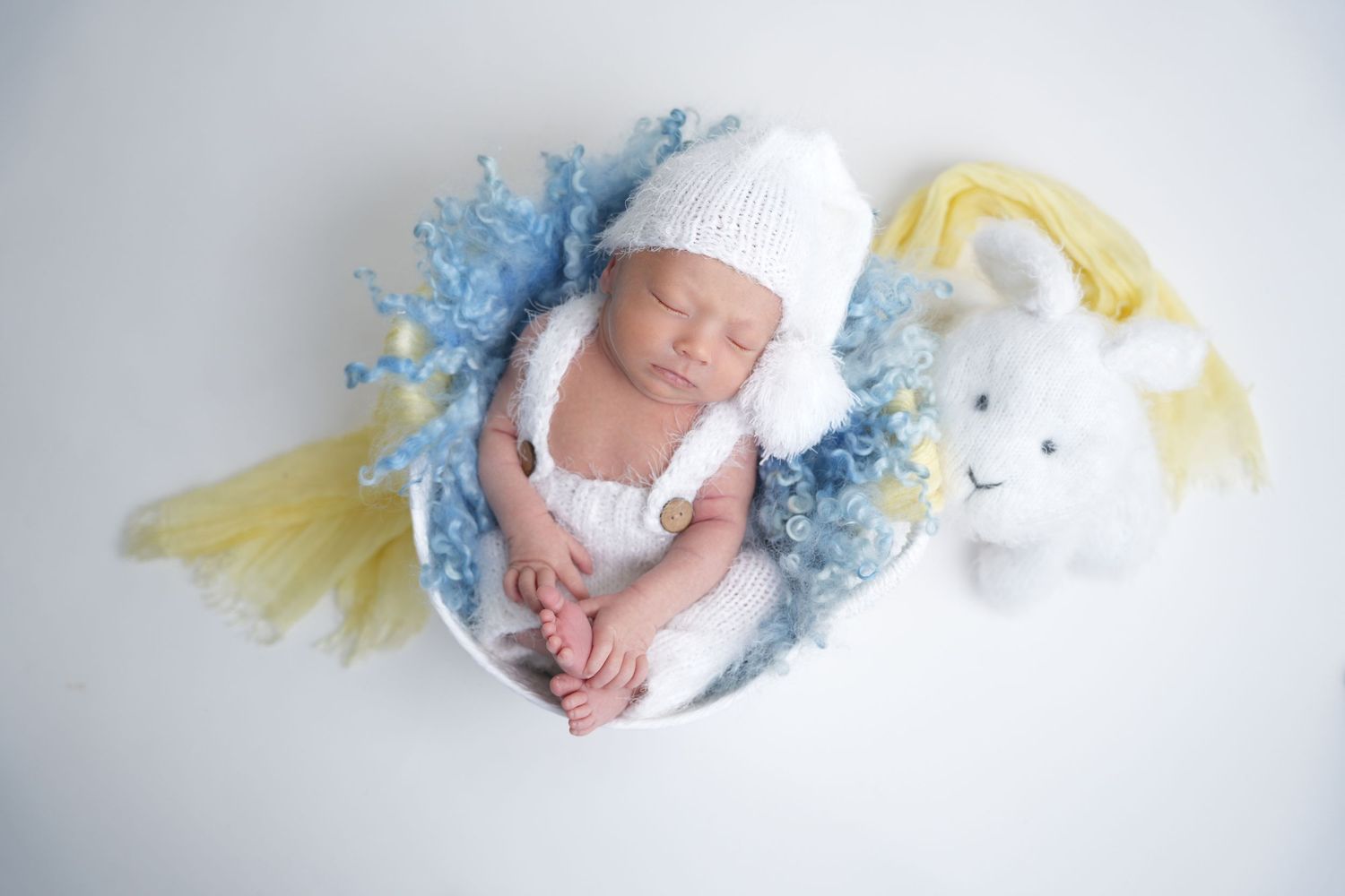 Sleeping newborn in white hat rests peacefully with blue and yellow decor and plush bunny toy.
