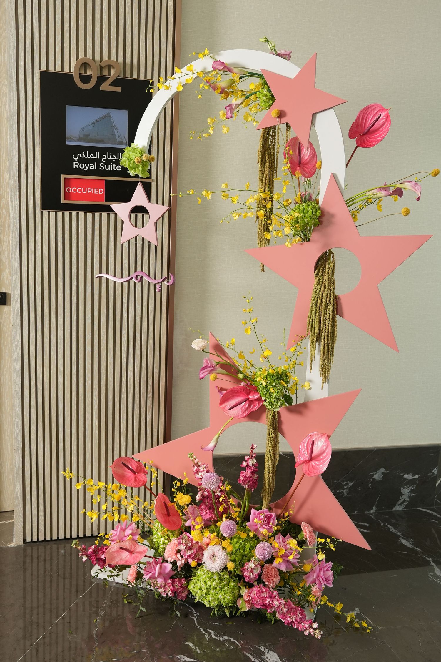 Modern floral arrangement with pink stars, cactus, and mixed flowers in fresh spring colors against a neutral wall.