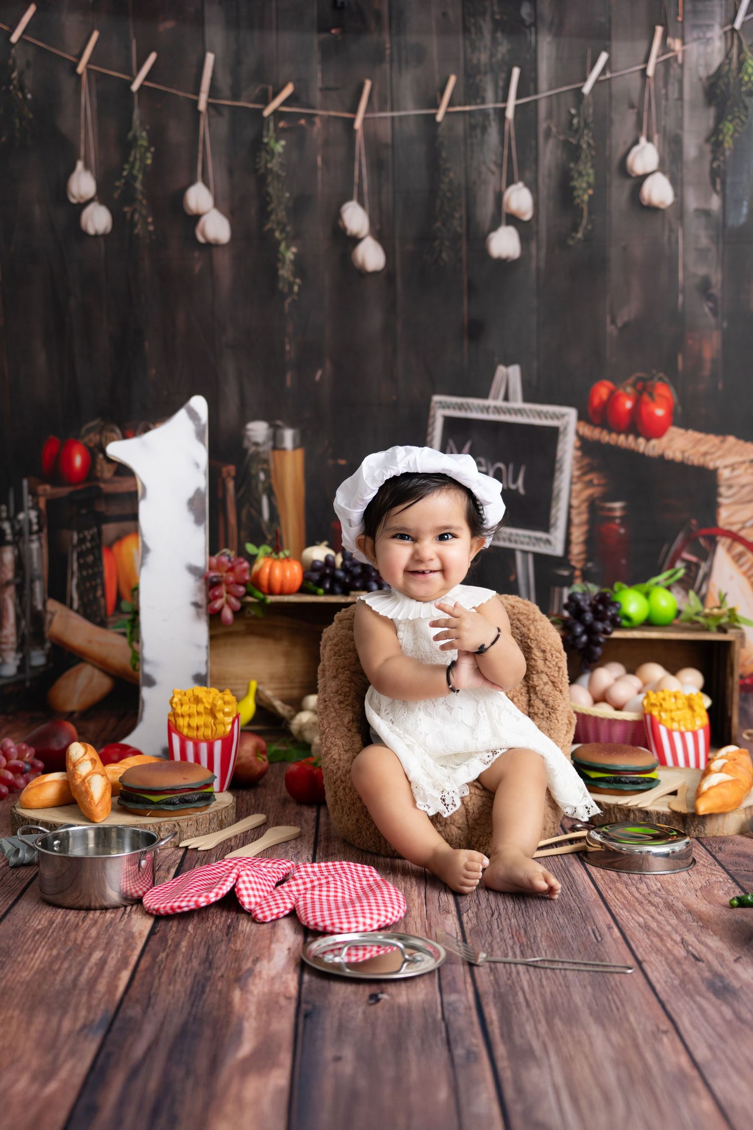 A series of four photos showing a baby in a white dress with teddy bear and snacks on a rustic wooden table setting.