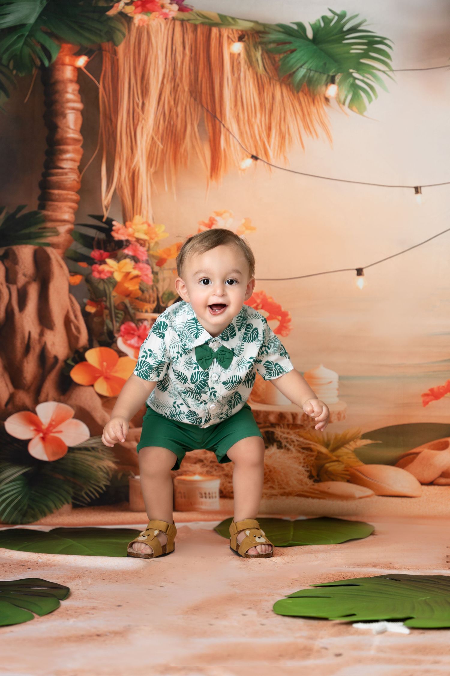 A baby in a tropical-themed photo set crawls and plays among palm leaves and hibiscus flowers.