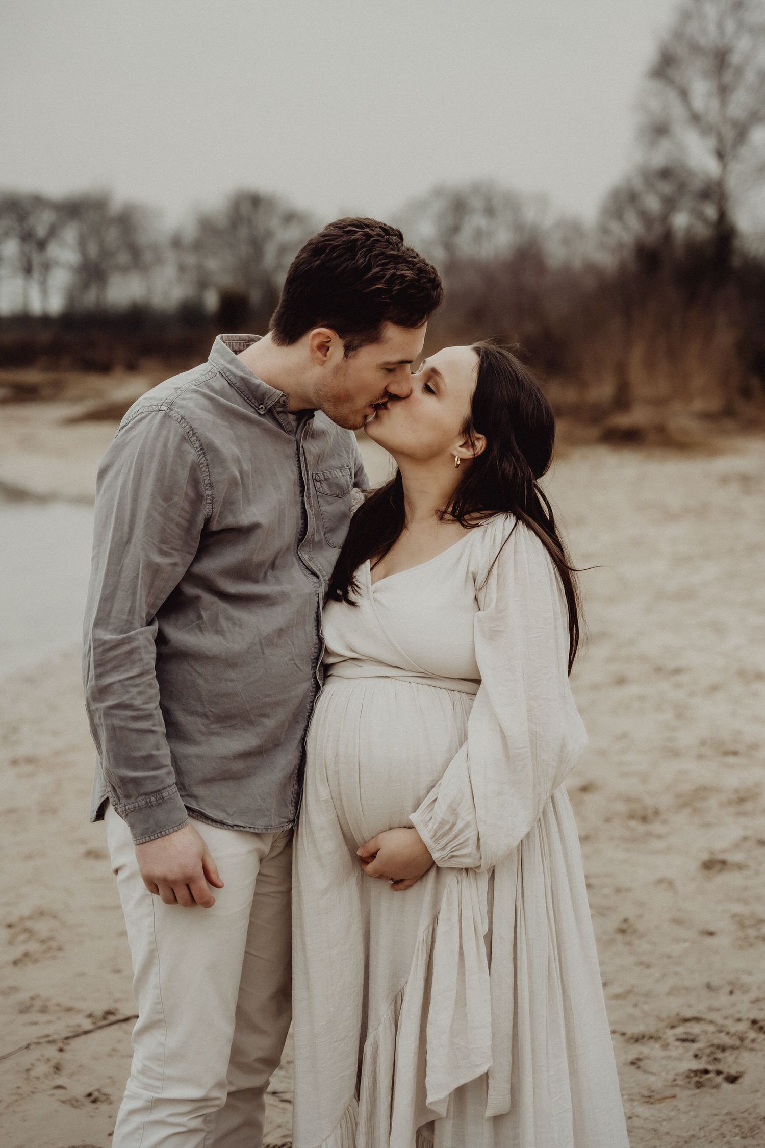 A couple shares an intimate moment on a sandy path during a maternity photoshoot.