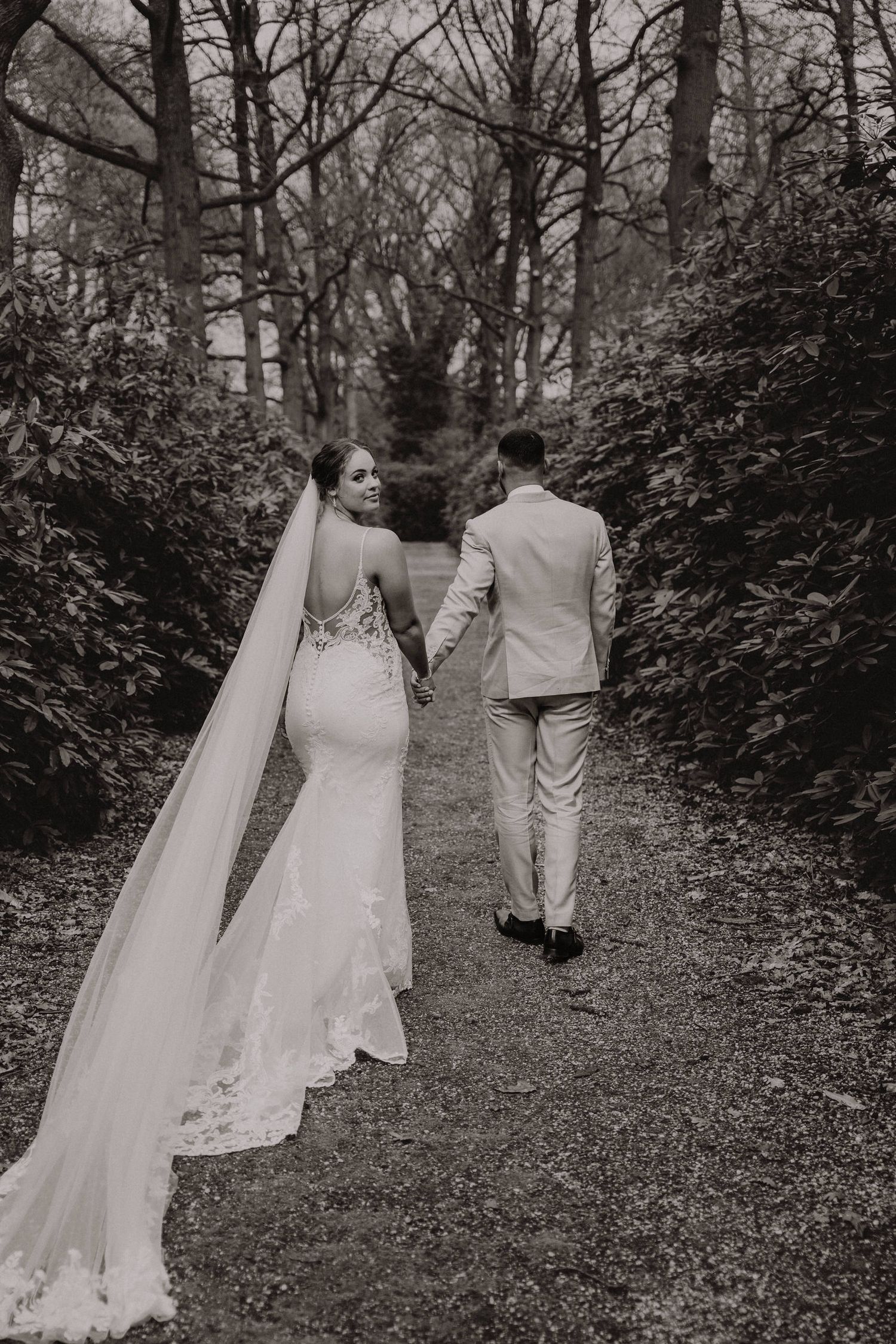 A couple walks hand in hand down a forest path surrounded by trees.