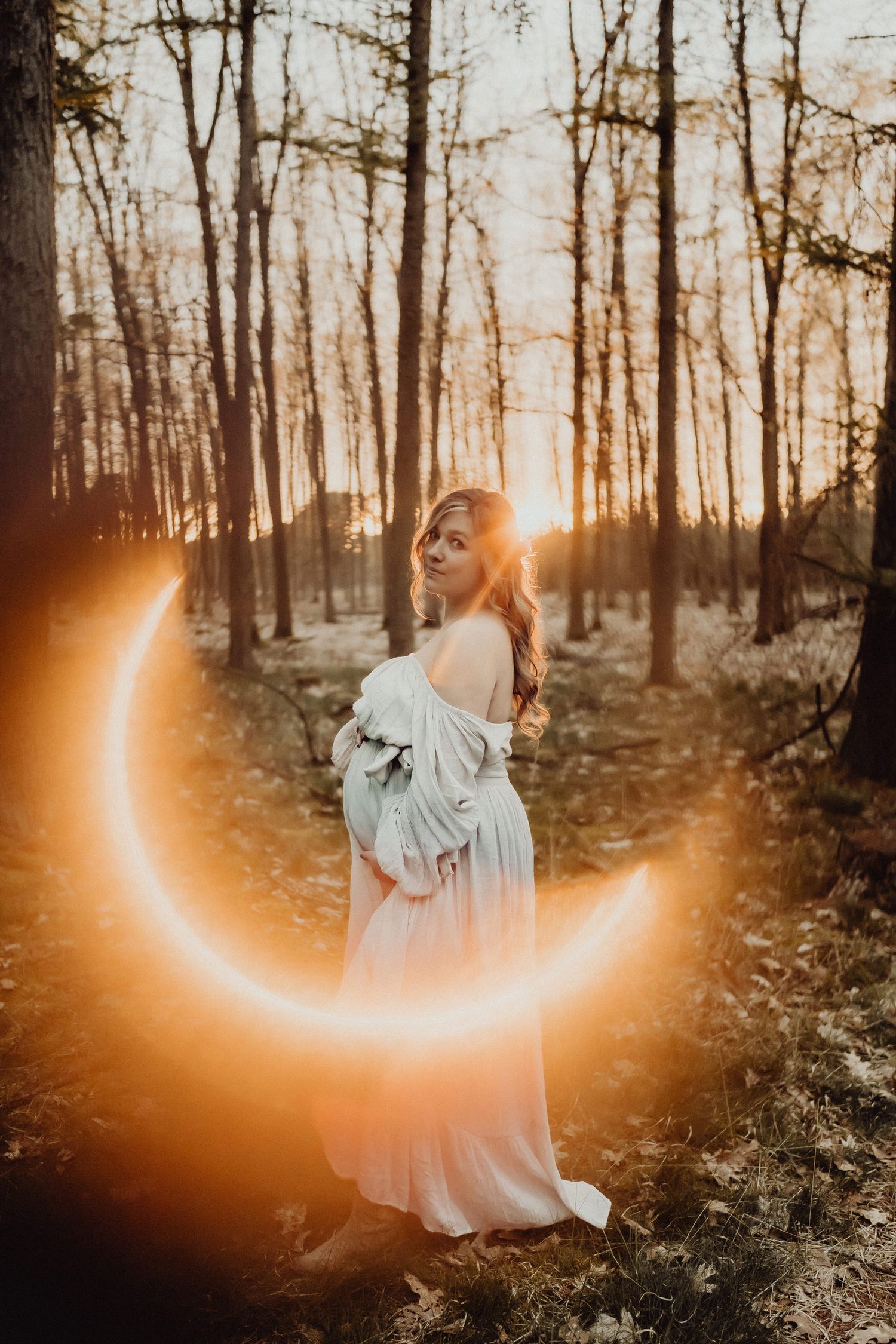 Ethereal sunset maternity photo in a forest with a glowing crescent moon light effect.