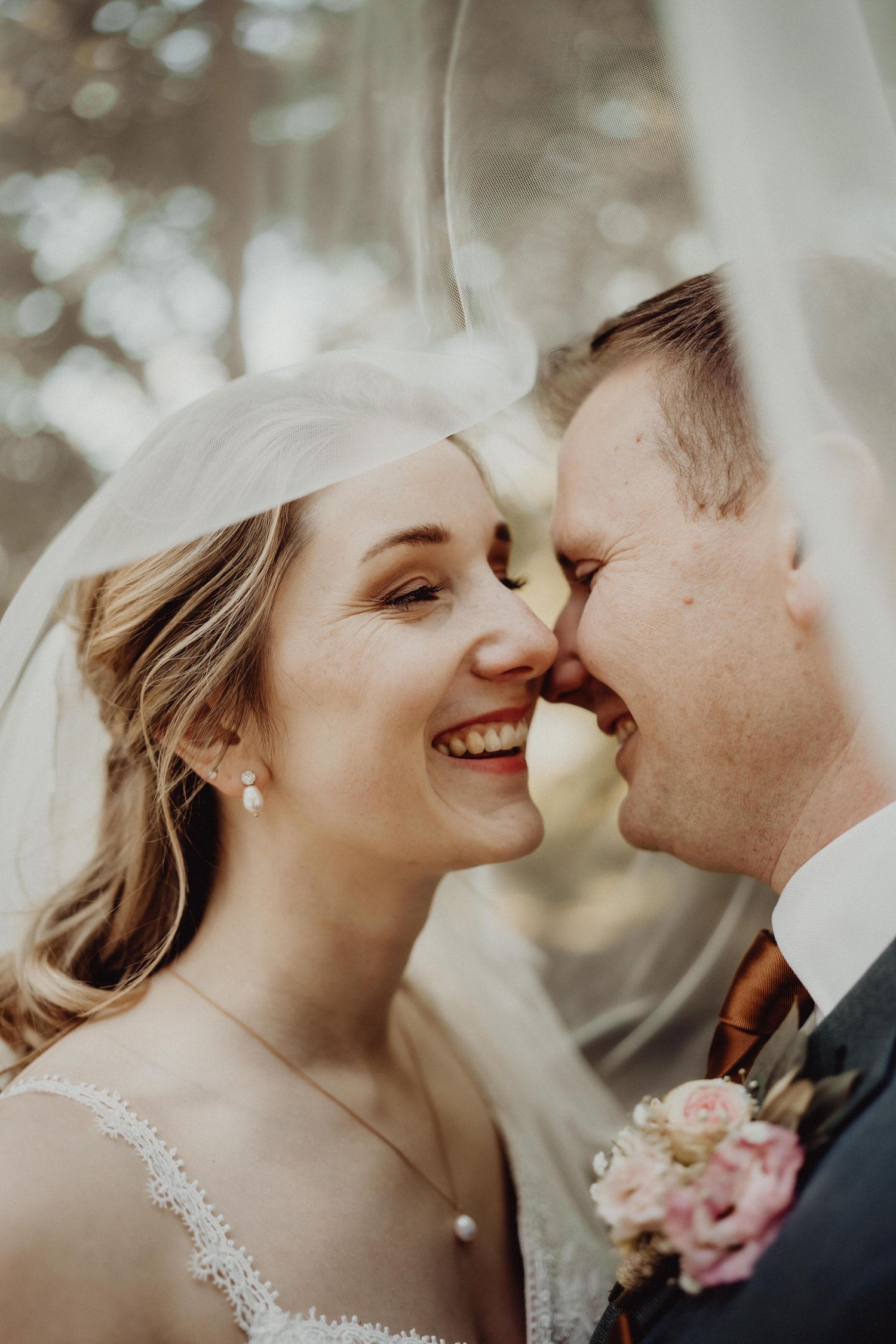 Intimate closeup of newlyweds sharing a joyful moment under bridal veil.