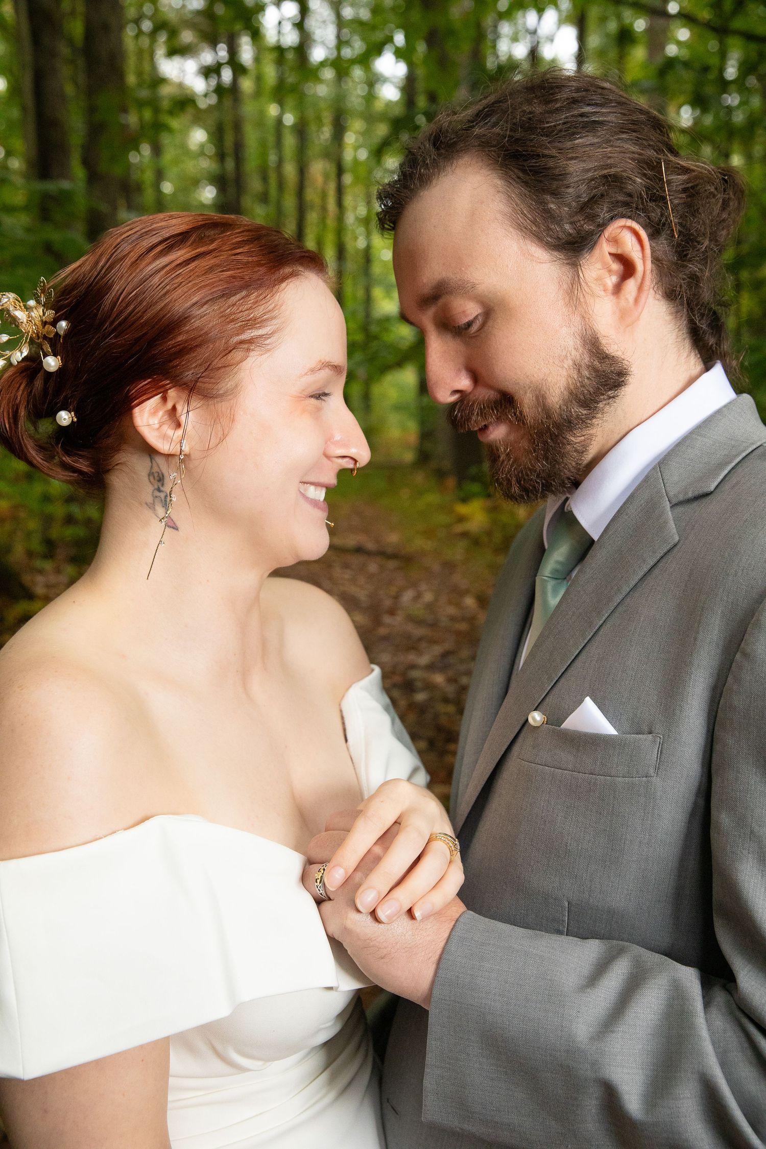 A romantic moment between a couple in formal attire standing together in a wooded outdoor setting.