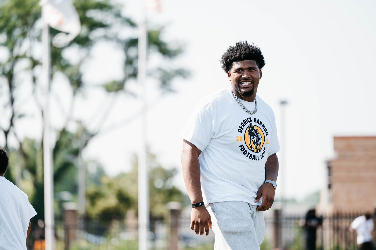 A smiling man wearing a white football team t-shirt stands outdoors on a sunny day.