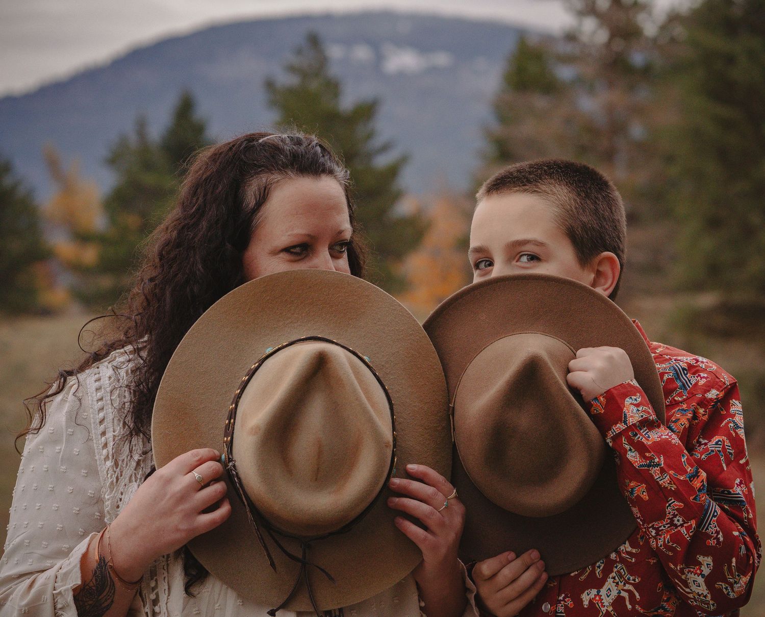 Two people peek over the brims of matching tan cowboy hats in an autumn field.