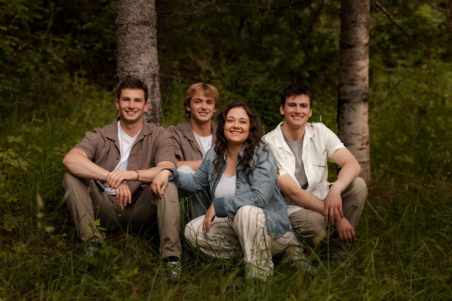 Four young adults smiling and sitting together in a lush green forest setting for a group photo.
