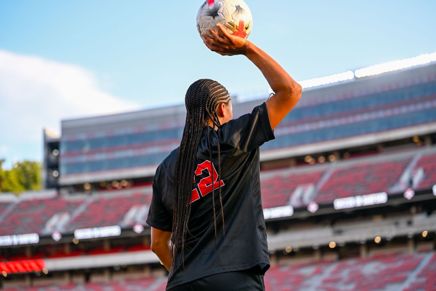 Soccer player wearing number 2 jersey holds ball overhead in empty stadium during pre-game warmup.