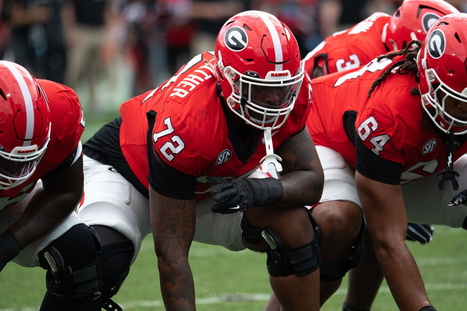Football offensive line in red jerseys crouched in formation before snap.