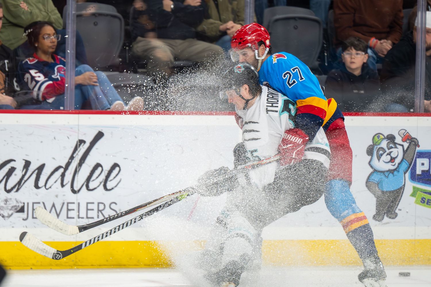 Ice hockey player sprays snow while making an abrupt stop on the rink during intense gameplay.