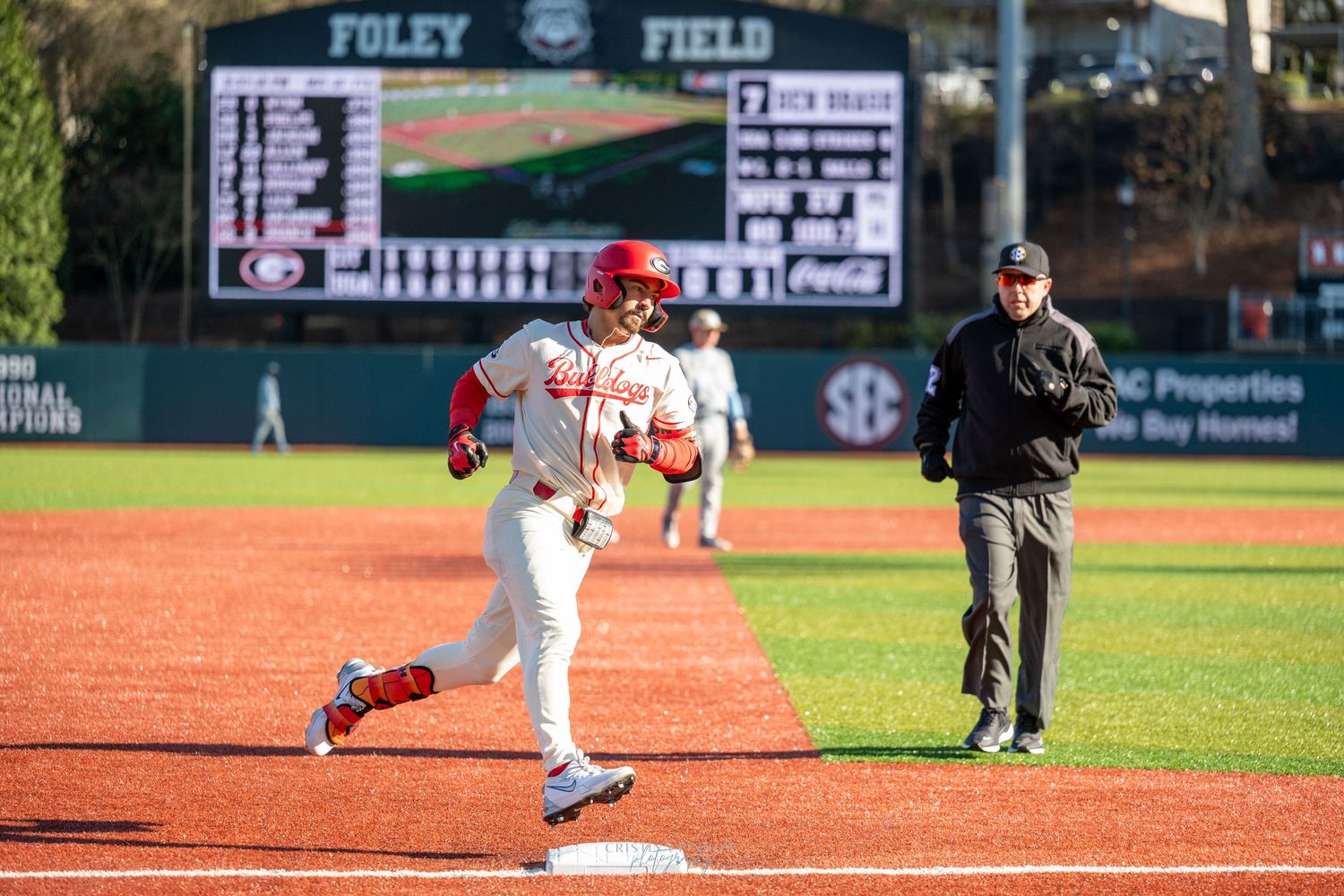 Baseball player rounds third base at Foley Field during an SEC game, with an umpire watching nearby.