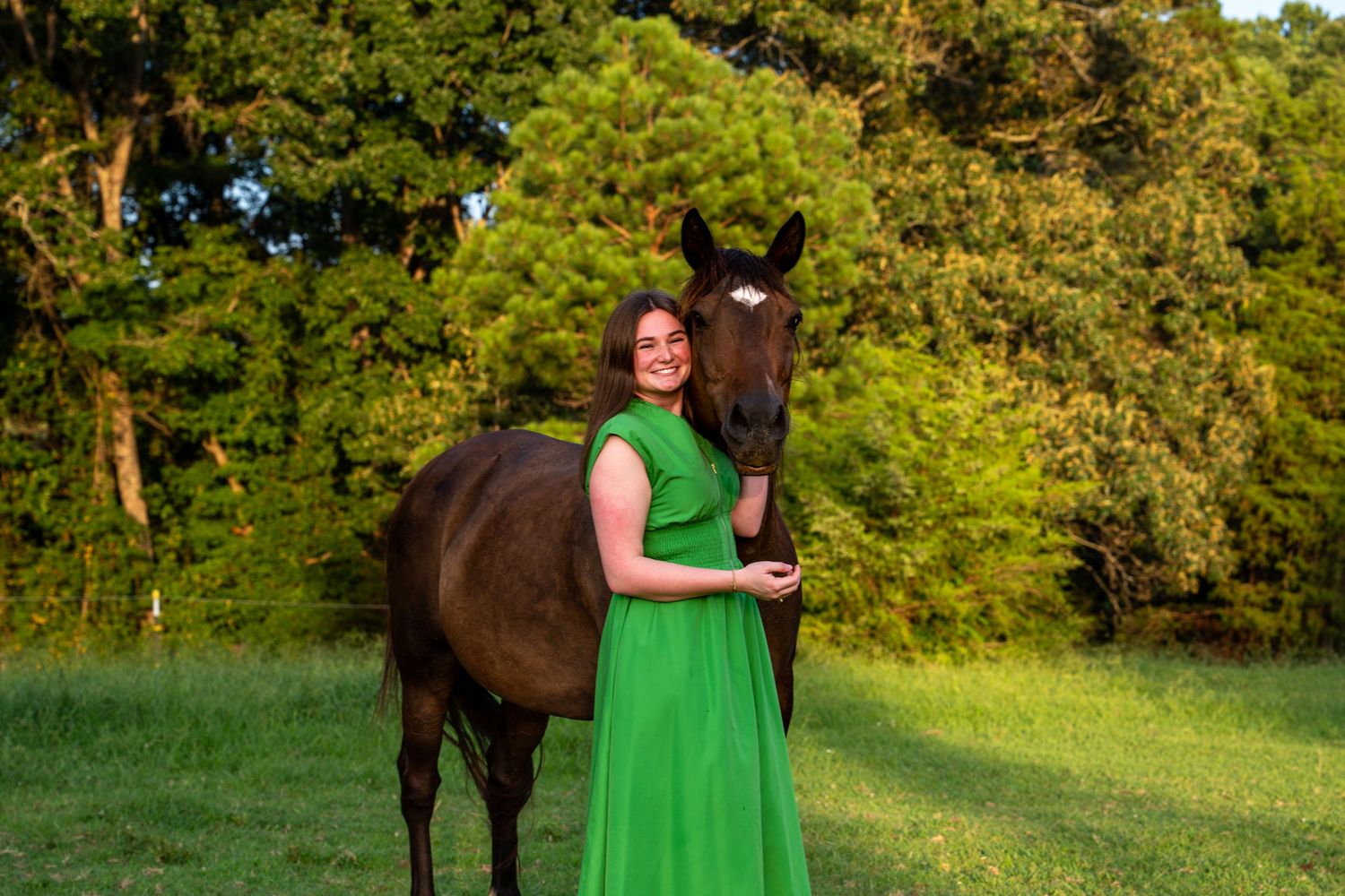 Person in bright green dress standing with horses in a sunny field.