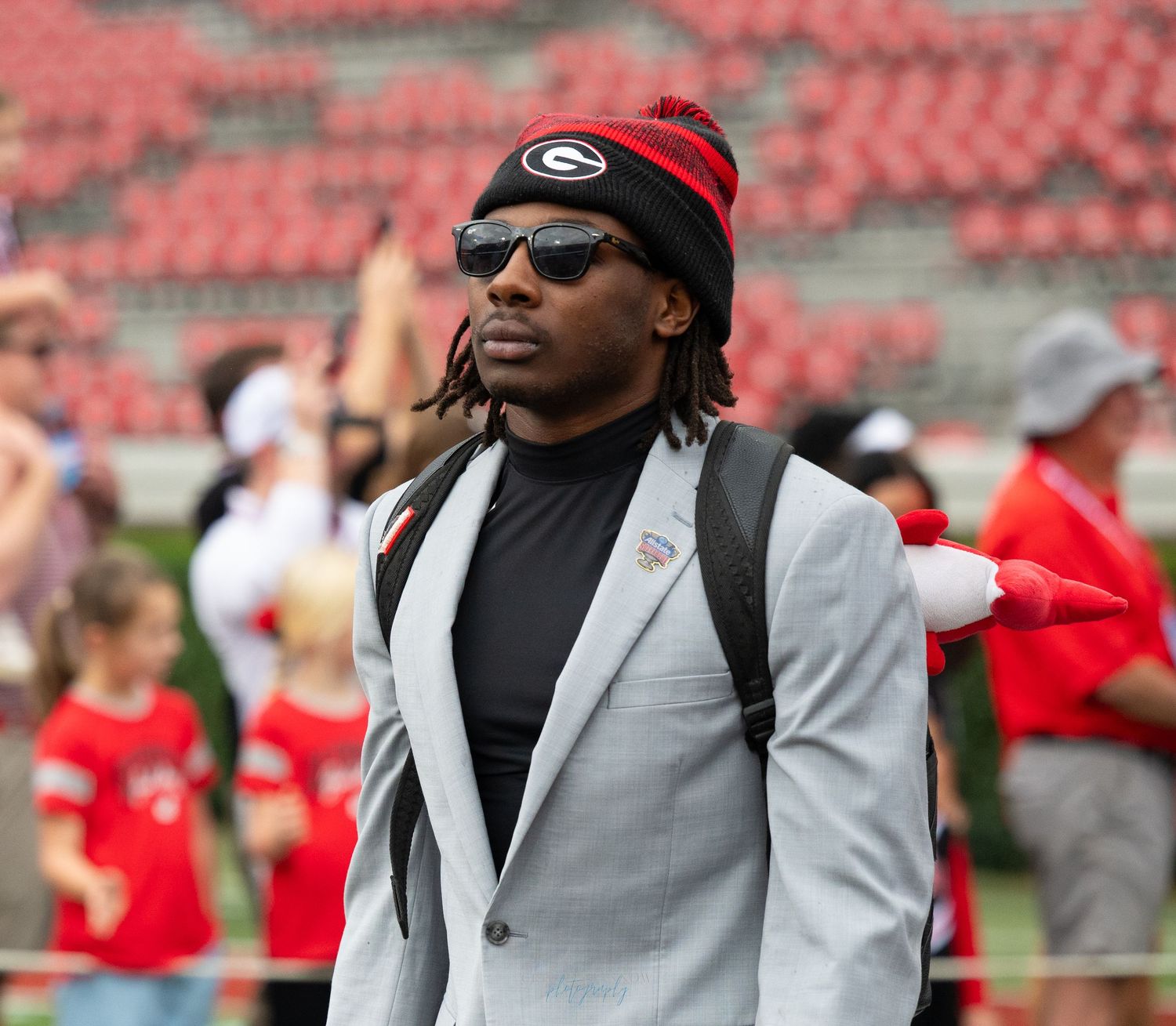 People in formal attire at a sports stadium with red seats visible.