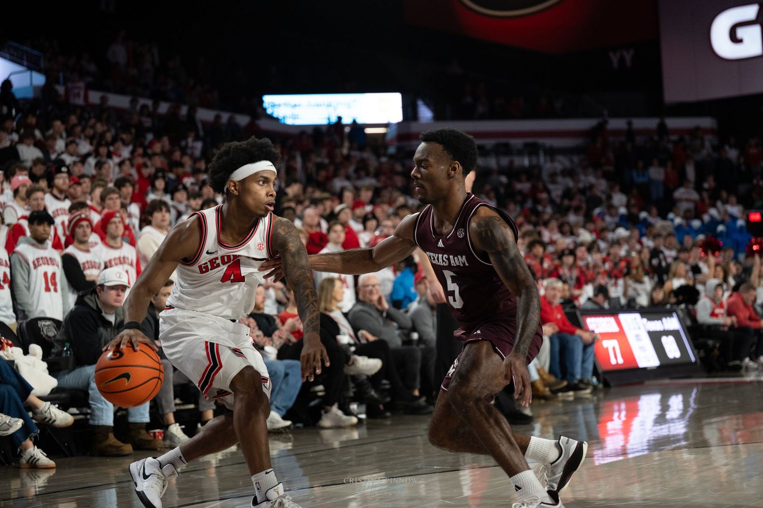 Two basketball players face off during an intense game with one player dribbling while the other defends.