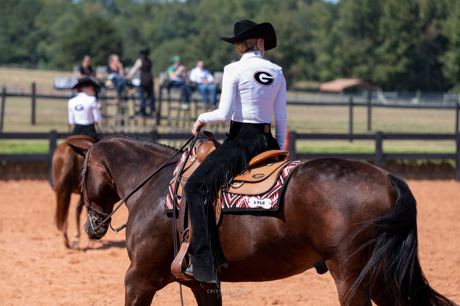 A rider in western attire on horseback wearing a black hat and white shirt with G logo.