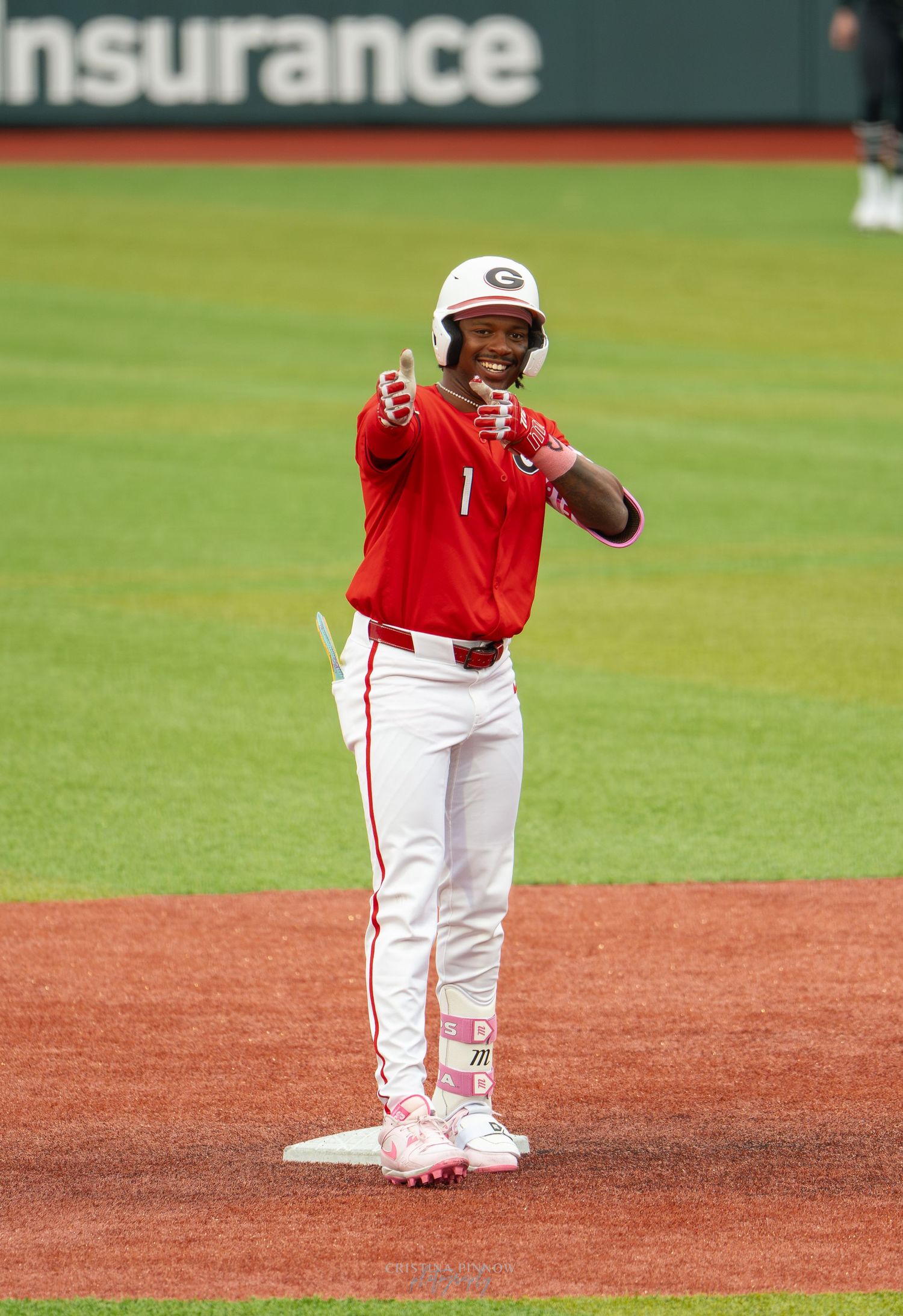 Baseball player in red uniform pointing fingers at second base during a college game.