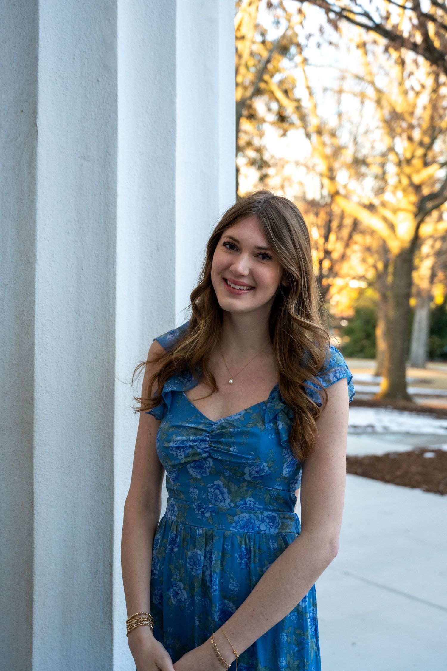 Person in a blue dress poses between white columns during golden hour.