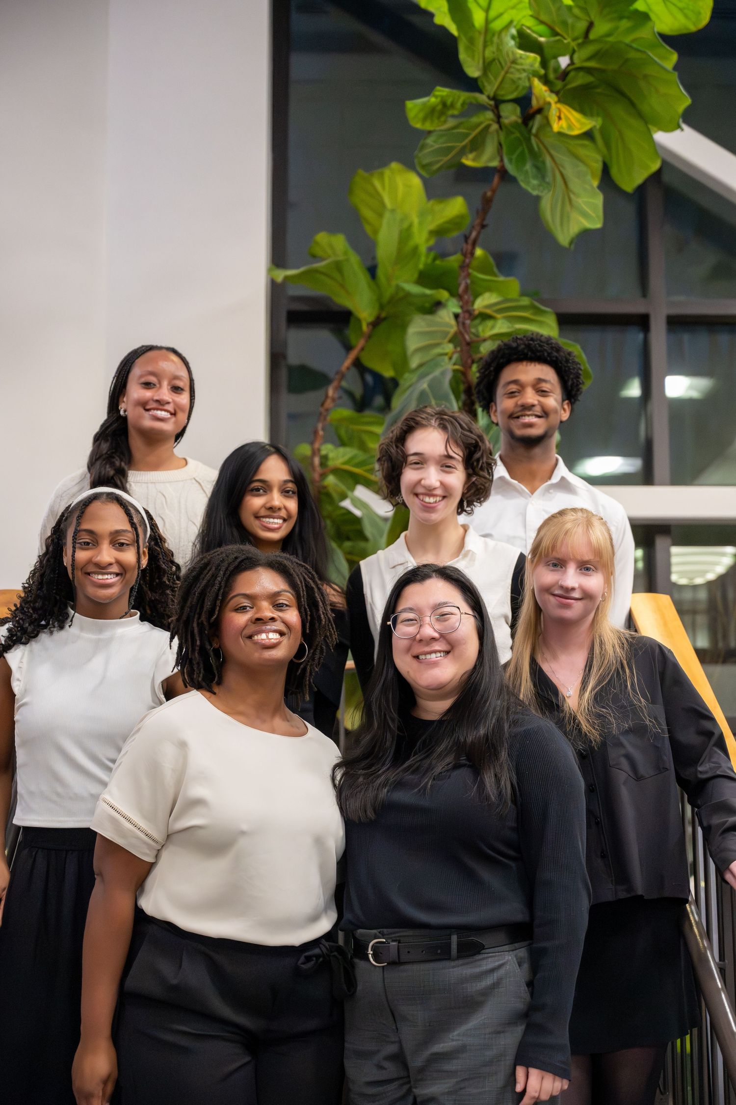 Diverse group of students smiling together in front of a green plant.