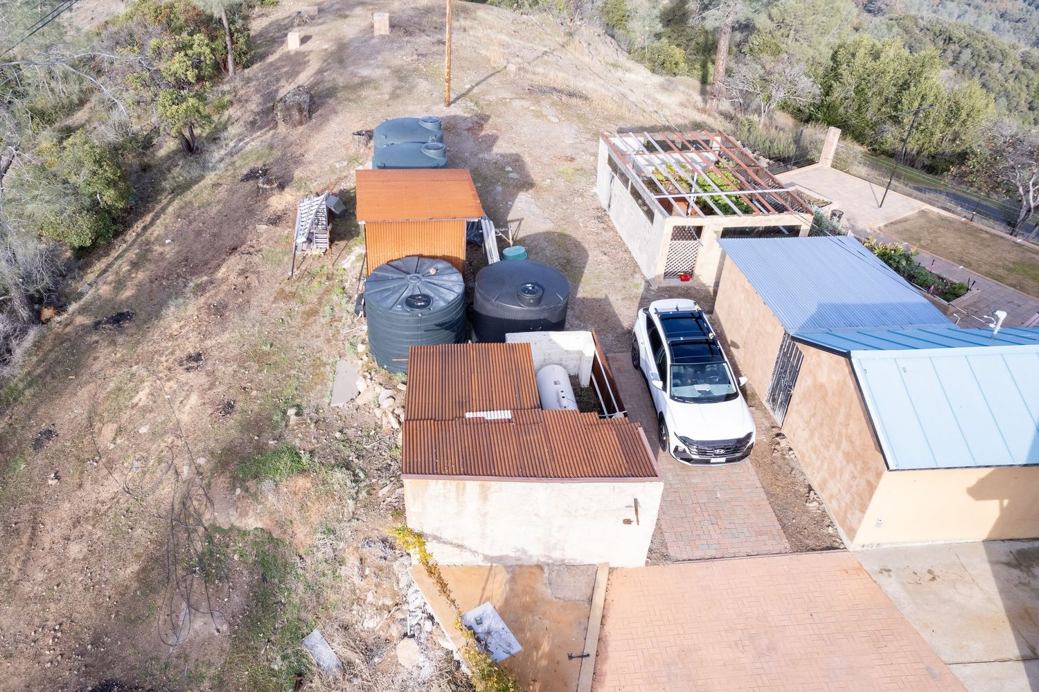 Wide aerial view of Forest Ranch residential property showing house, outbuildings, and vehicles. Elevated drone shot