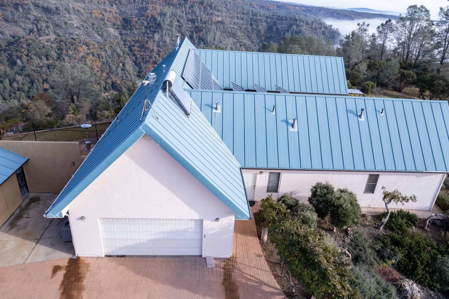 Aerial view of residential property with blue metal roof and solar panels in Forest Ranch California