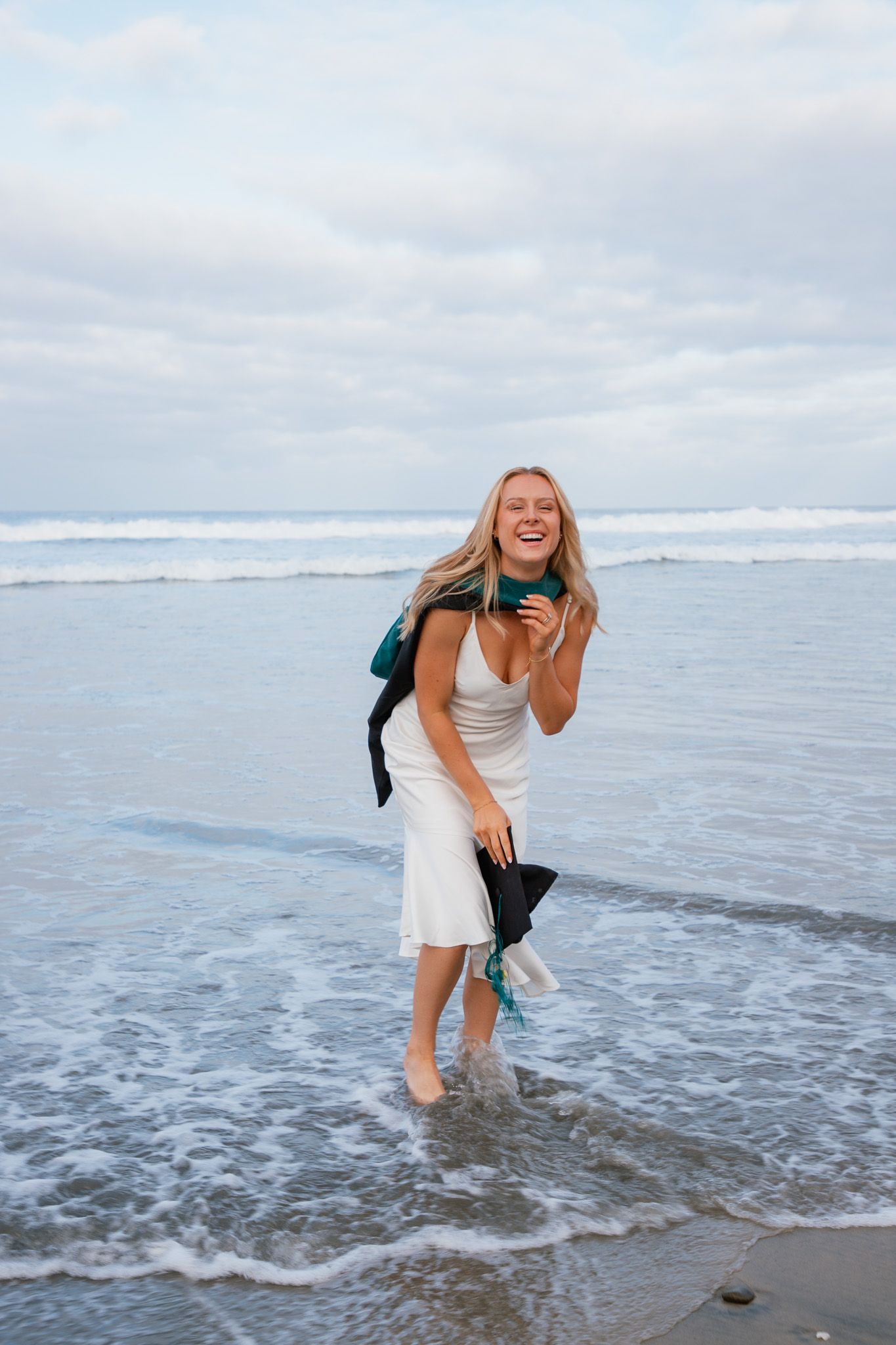 girl holding cap and gown after graduation walking on the beach