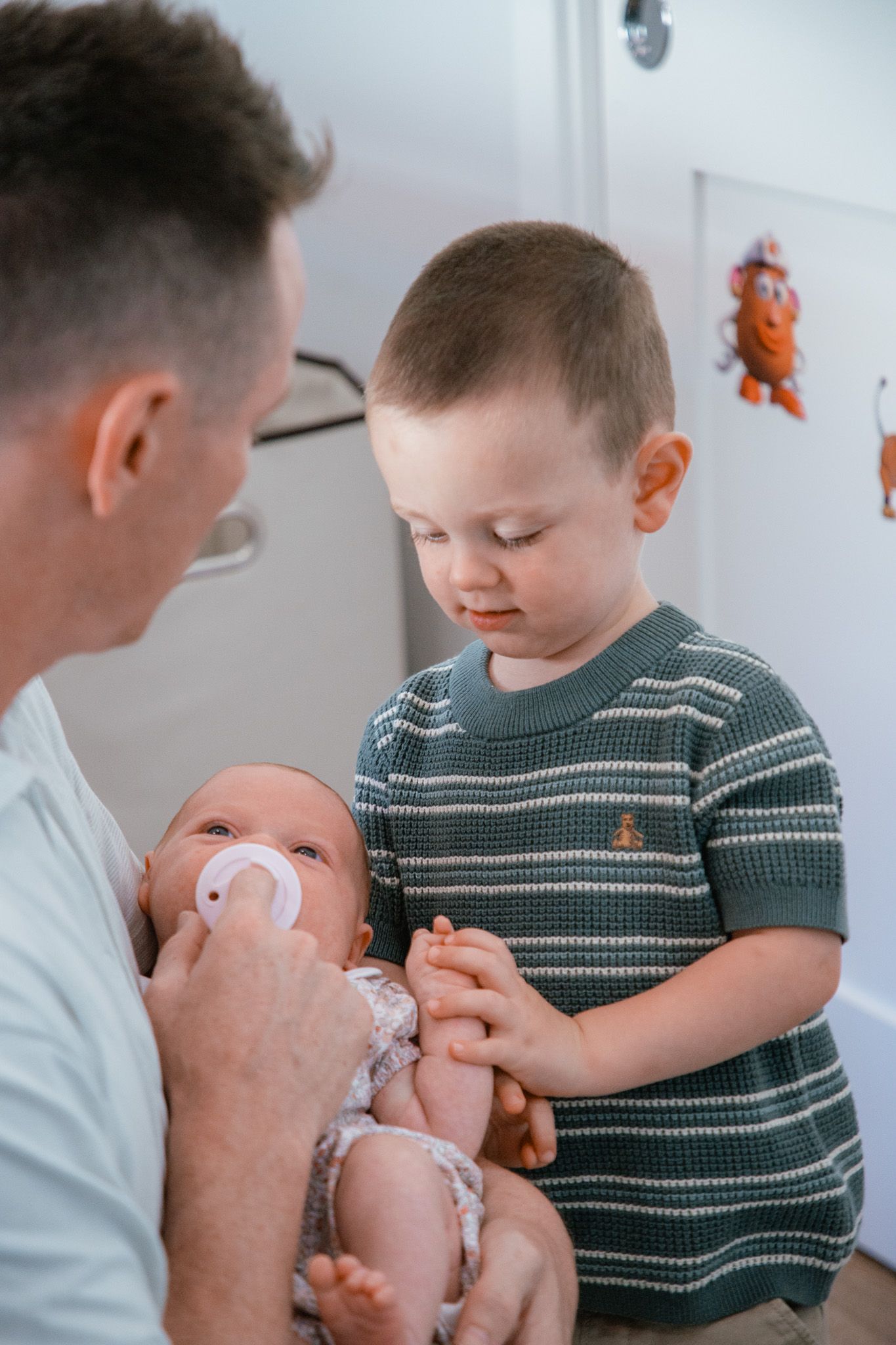 father and toddler son looking at their newborn baby girl