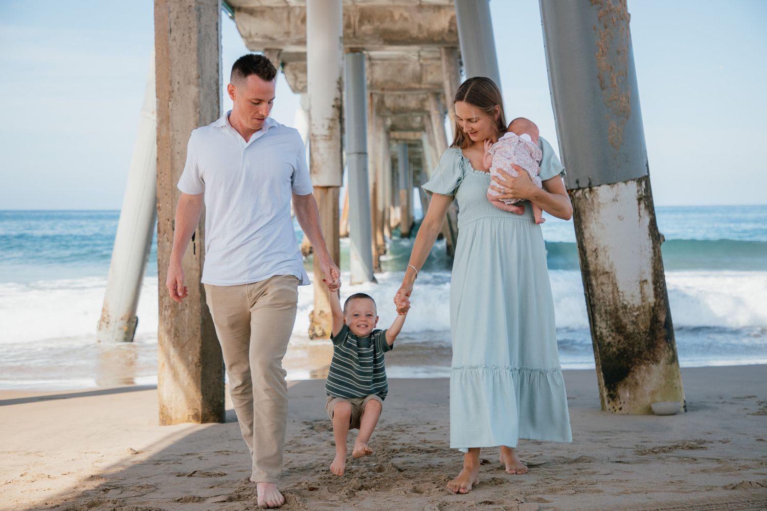 family with newborn and toddler holding hands under the pier
