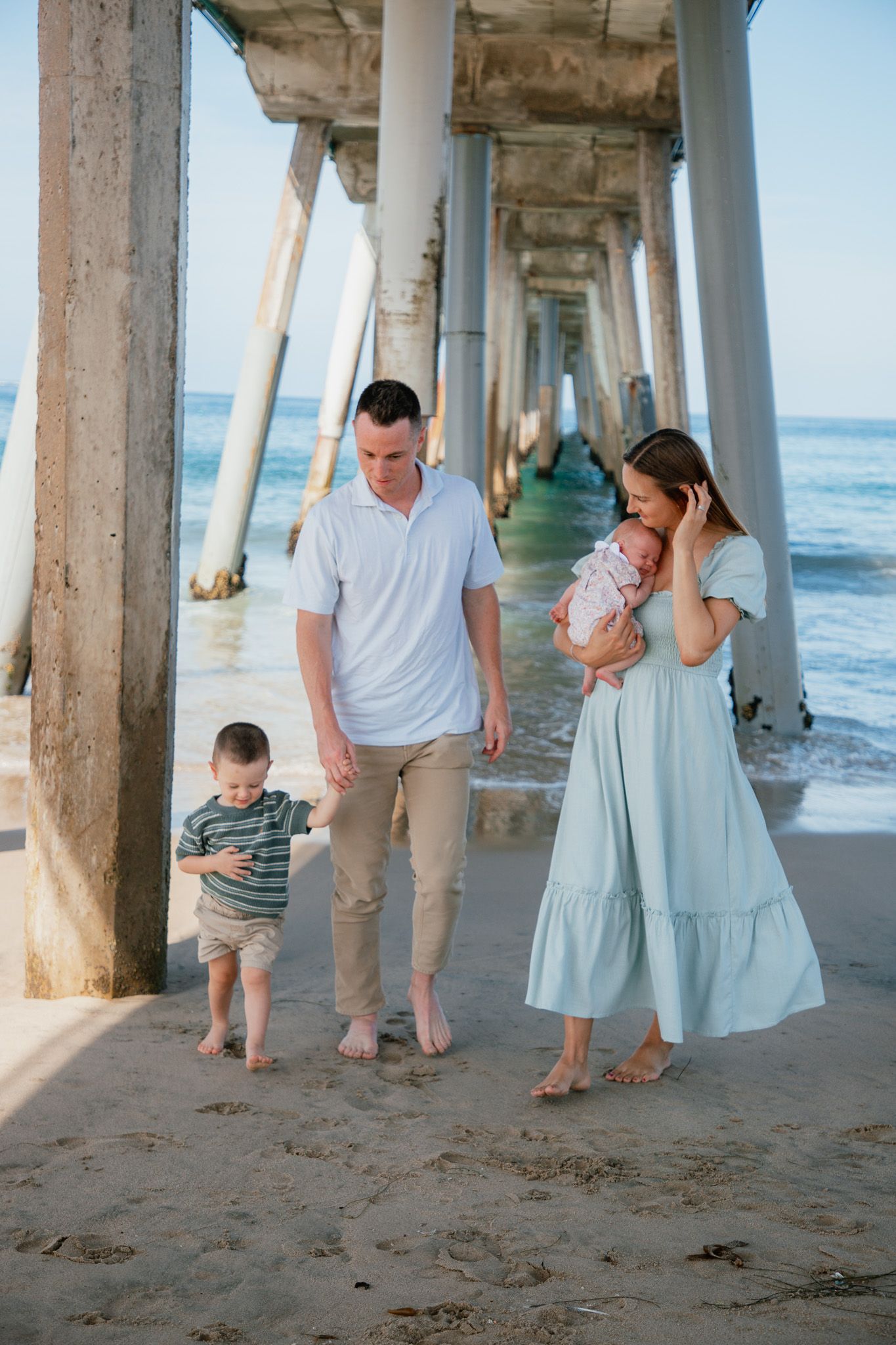 family with newborn and toddler holding hands under the pier