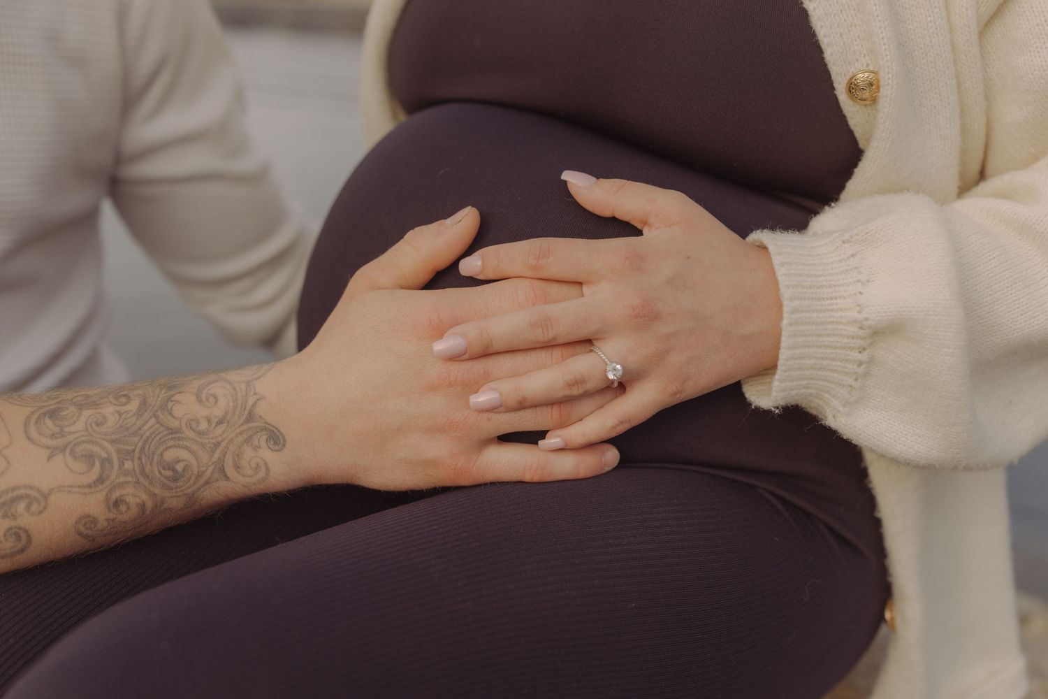 Close-up of pregnant woman's belly with hands gently resting on it, engagement ring visible.