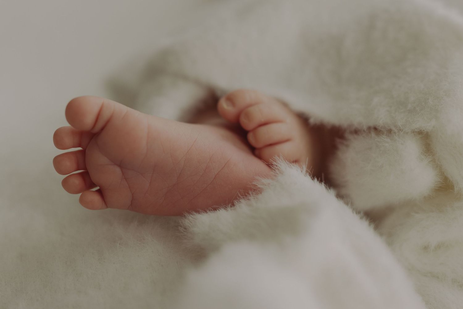 Close-up of a newborn baby's delicate tiny foot resting on a soft fluffy white blanket.