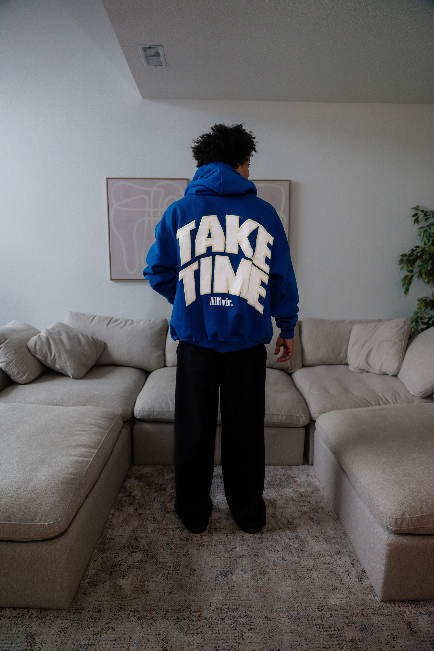Person wearing blue and white hoodie standing near gray couch in living room.