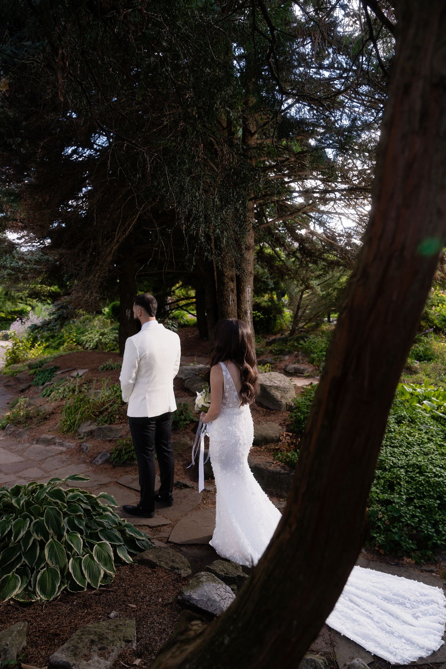Wedding couple walking through a scenic wooded path with trailing white dress.