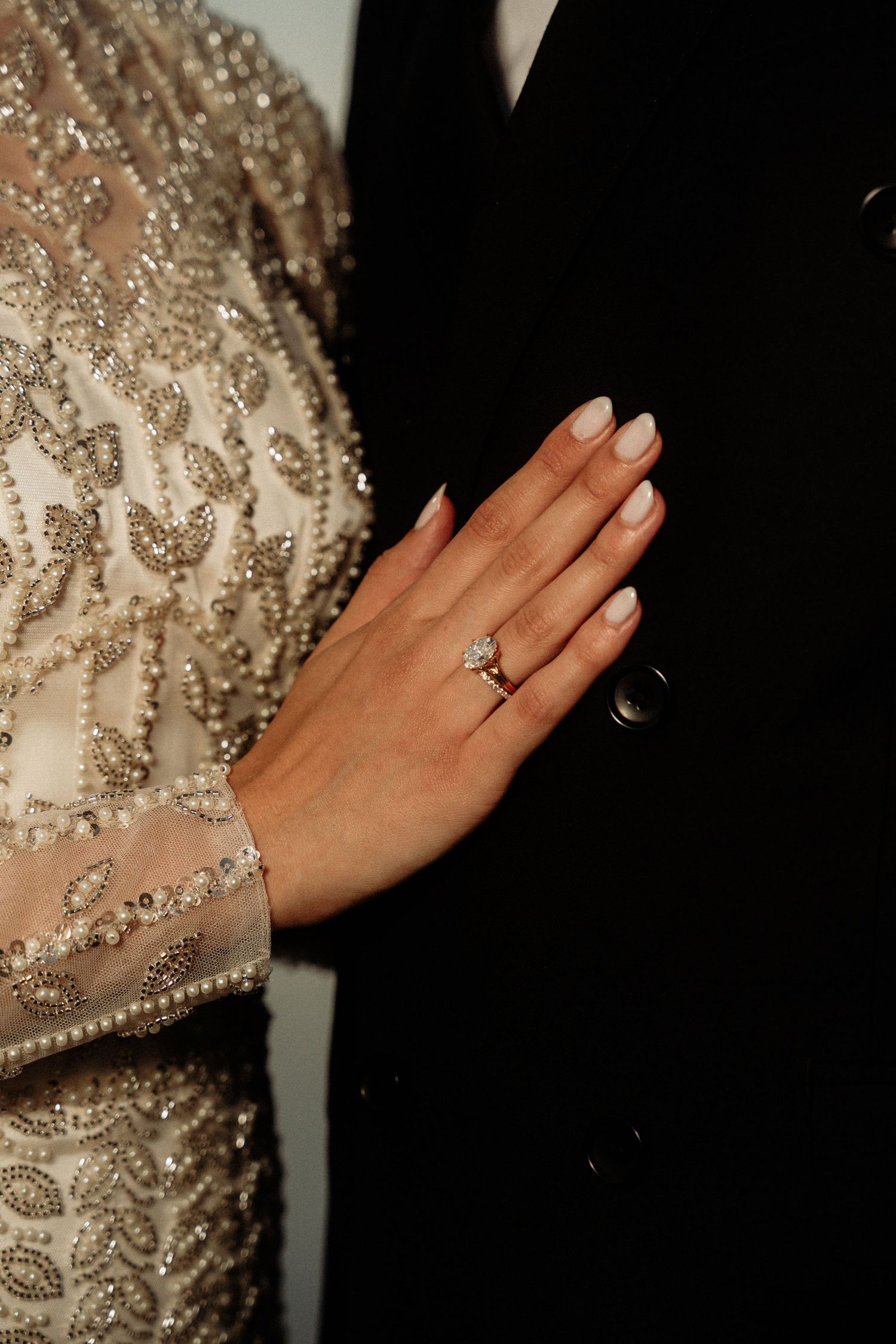 Close-up of a hand wearing an engagement ring against a beaded dress.
