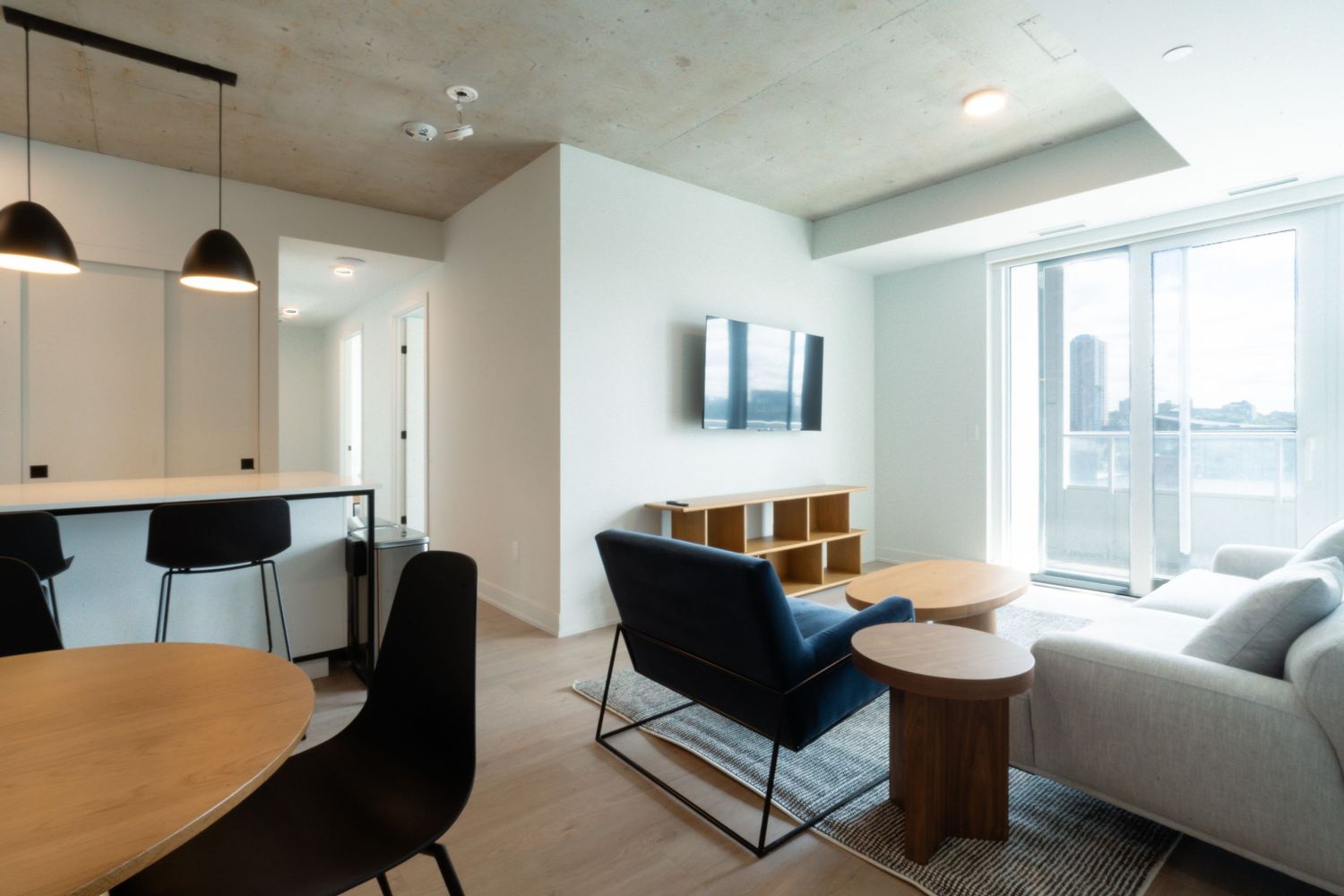 Modern minimalist office space with wooden desk and black chairs in a bright room with large windows.