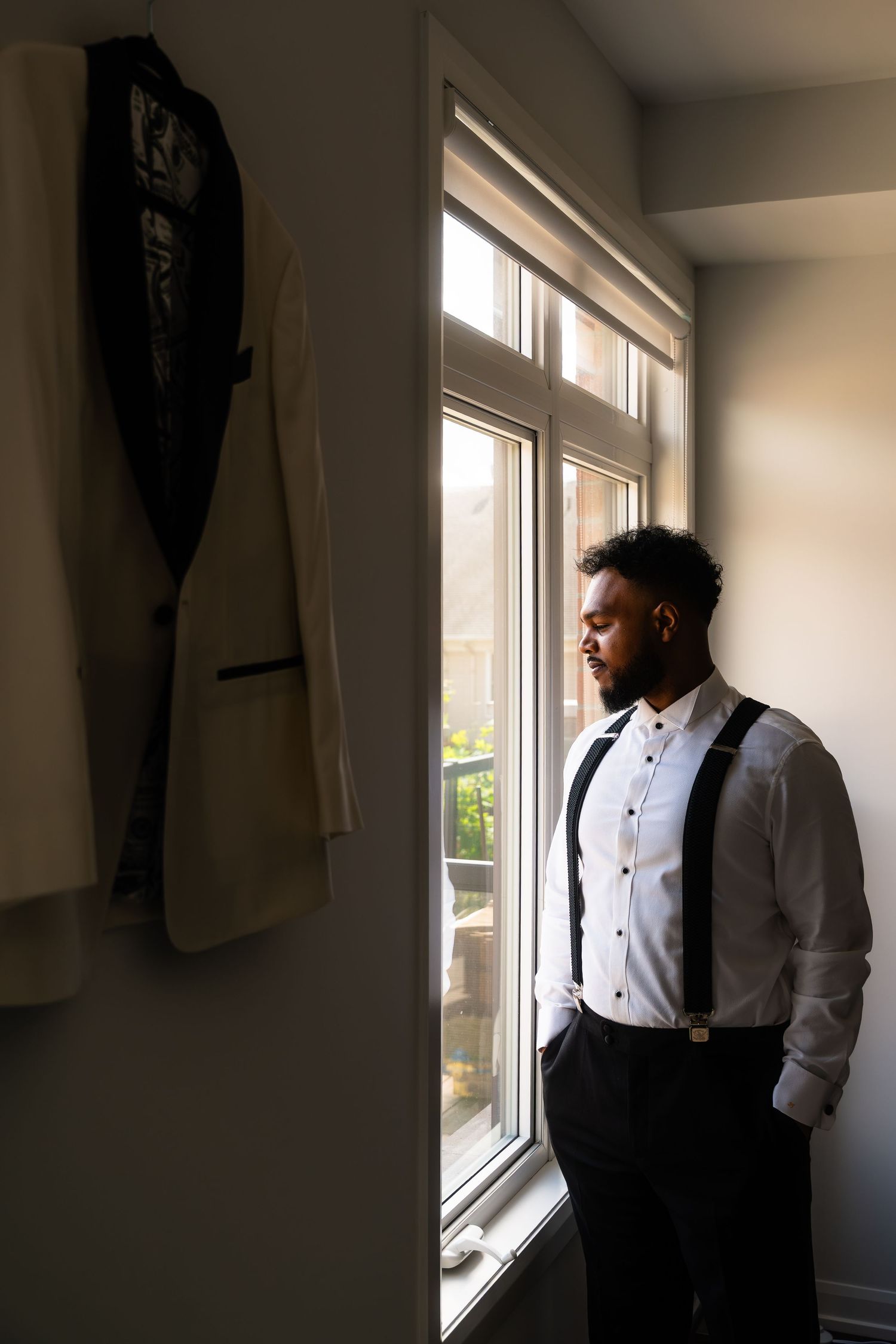A person in formal attire stands by a window in a minimalist room, creating a contemplative silhouette.