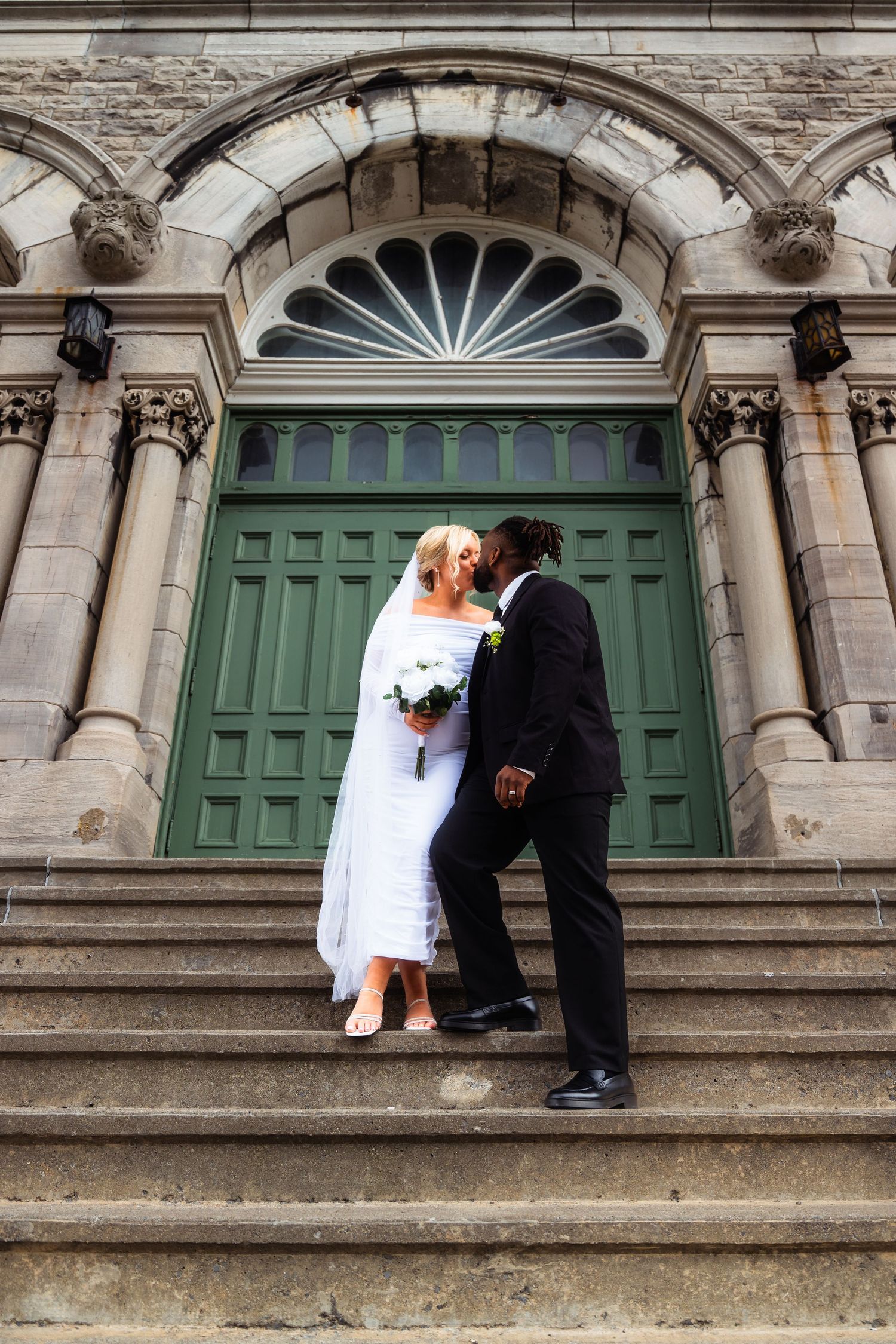 Newlyweds share an intimate moment on grand stone steps with ornate architectural details.