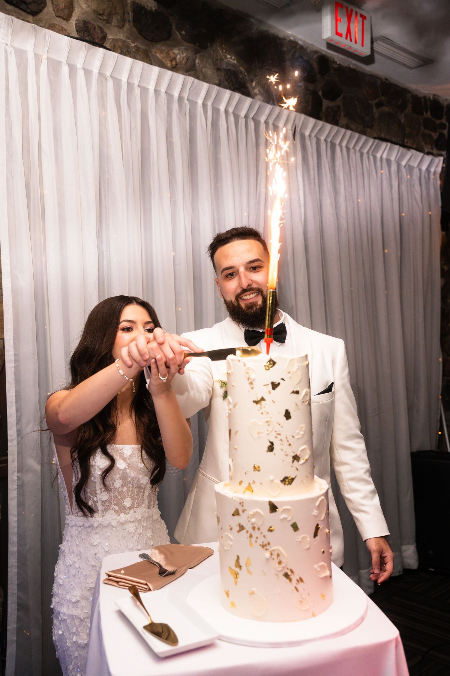 Wedding couple cuts into their elegant white and gold butterfly-themed cake at their reception celebration.