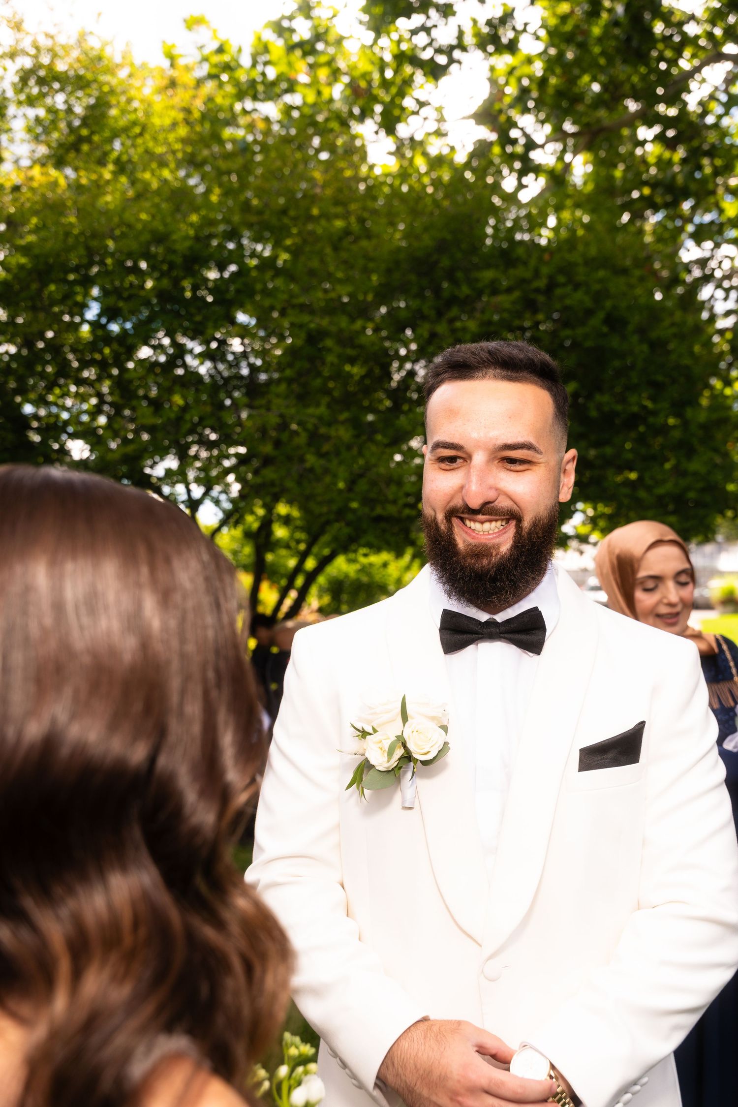 Wedding celebration with guests in formal attire gathered outdoors under trees.