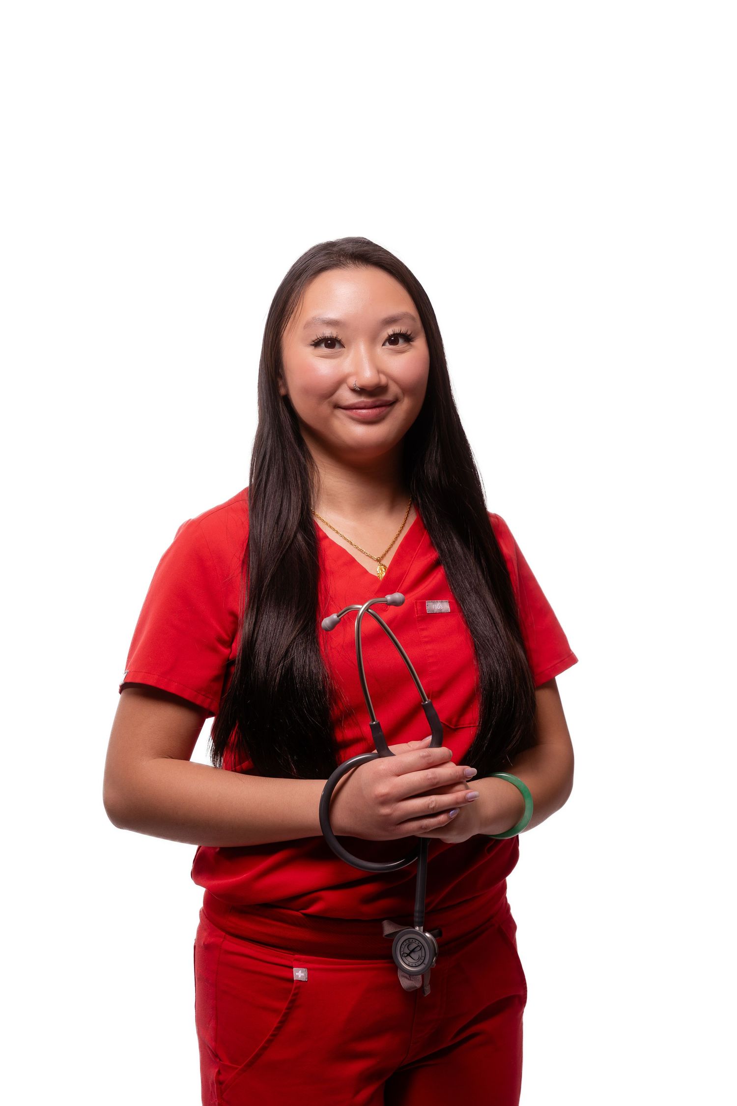 Medical professional in red scrubs holds stethoscope while smiling at camera.