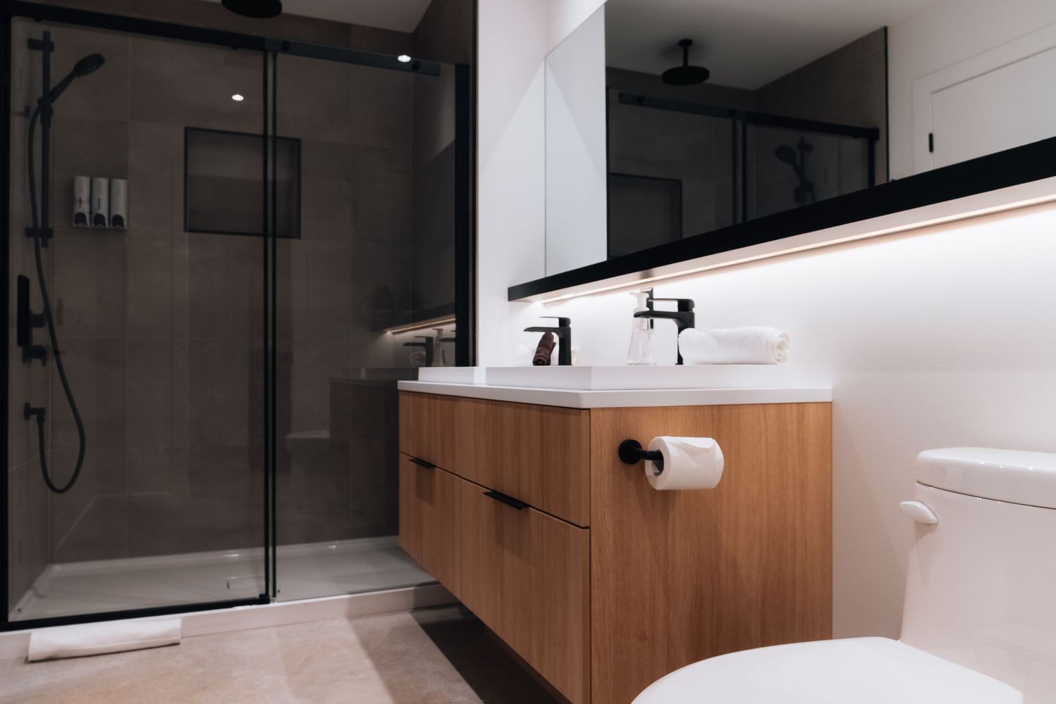 Minimalist bathroom design with dark glass shower enclosure and floating vanity in neutral tones.