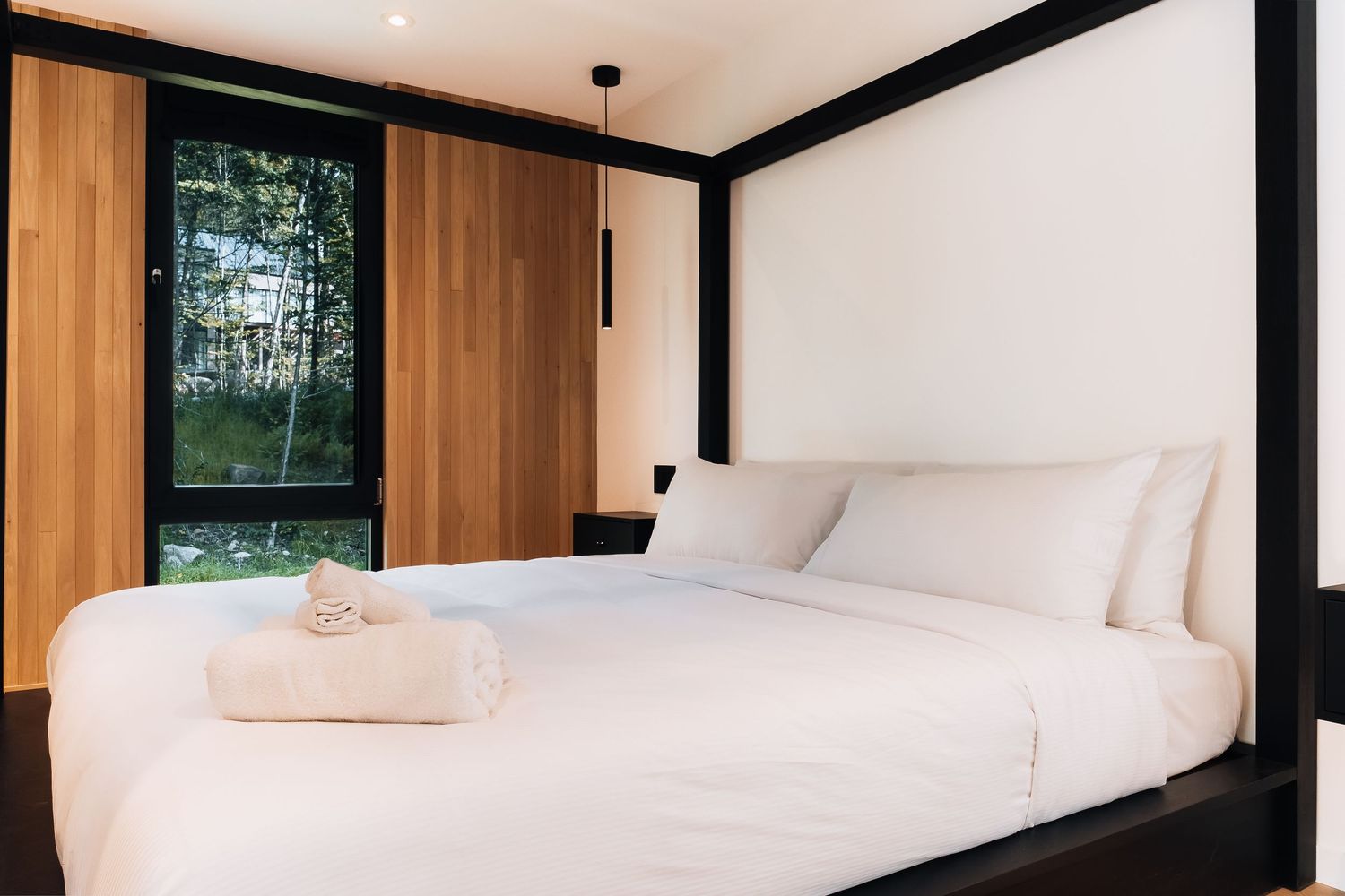 Clean white bedroom with wooden accents and natural light streaming through large windows.