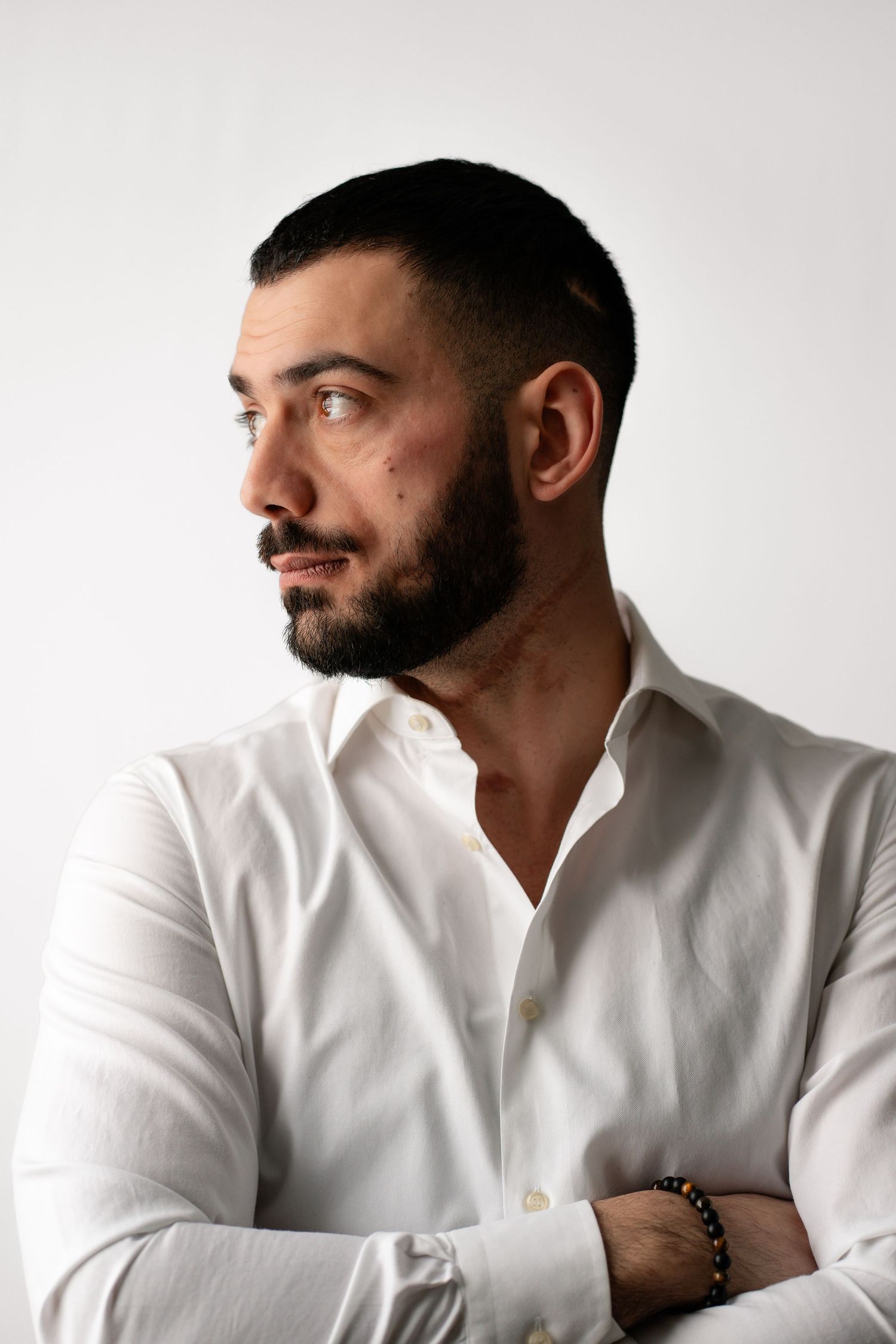 Side profile portrait of man in white shirt with beard against light background.