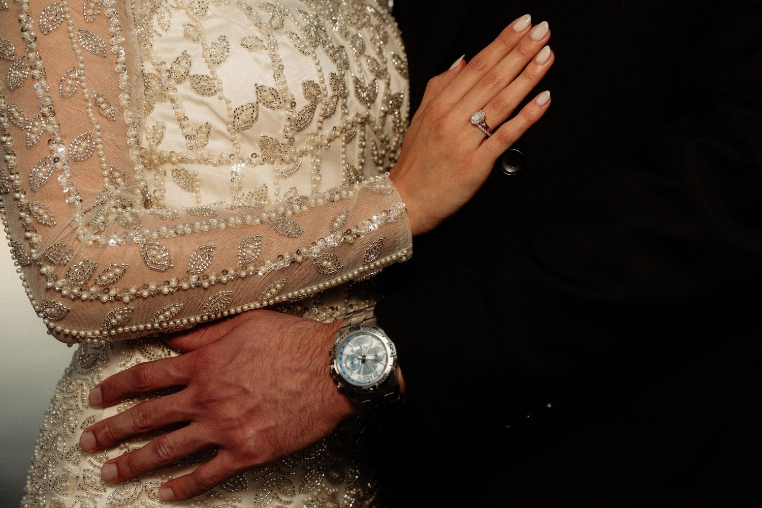 Intricate beadwork and pearls adorn a champagne-colored wedding gown in dramatic lighting.
