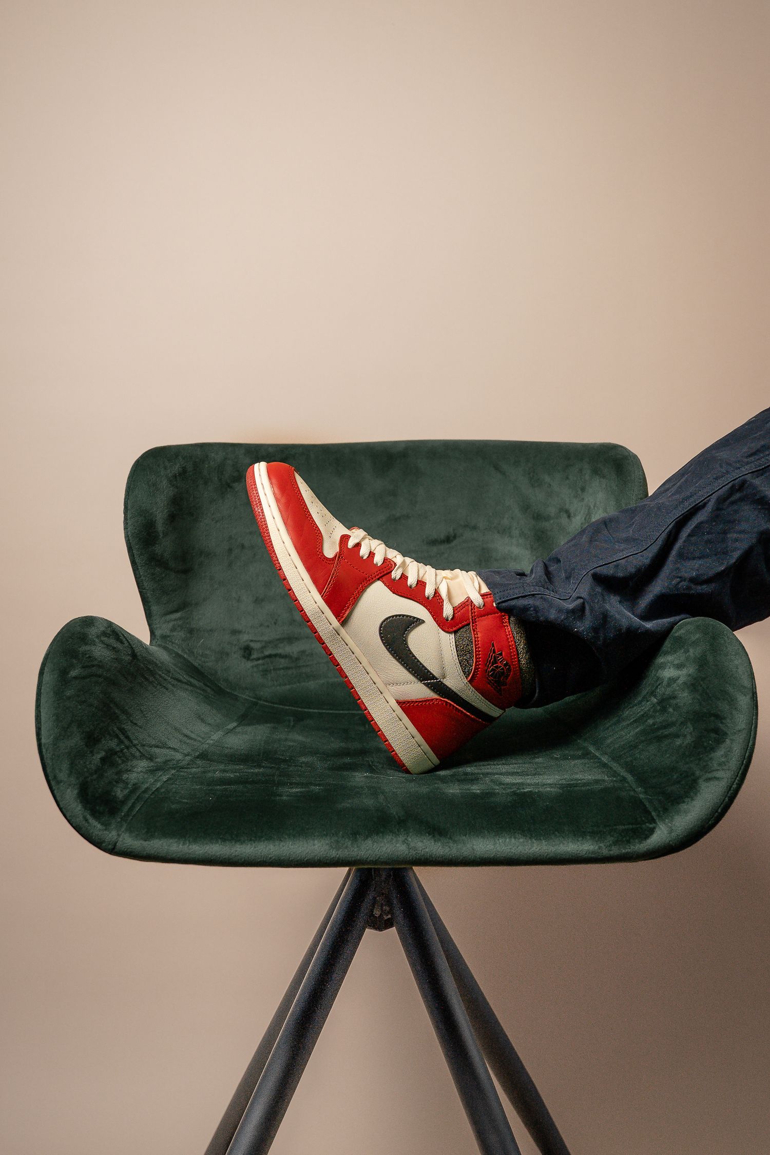 Red and white sneaker displayed on green velvet modern chair.