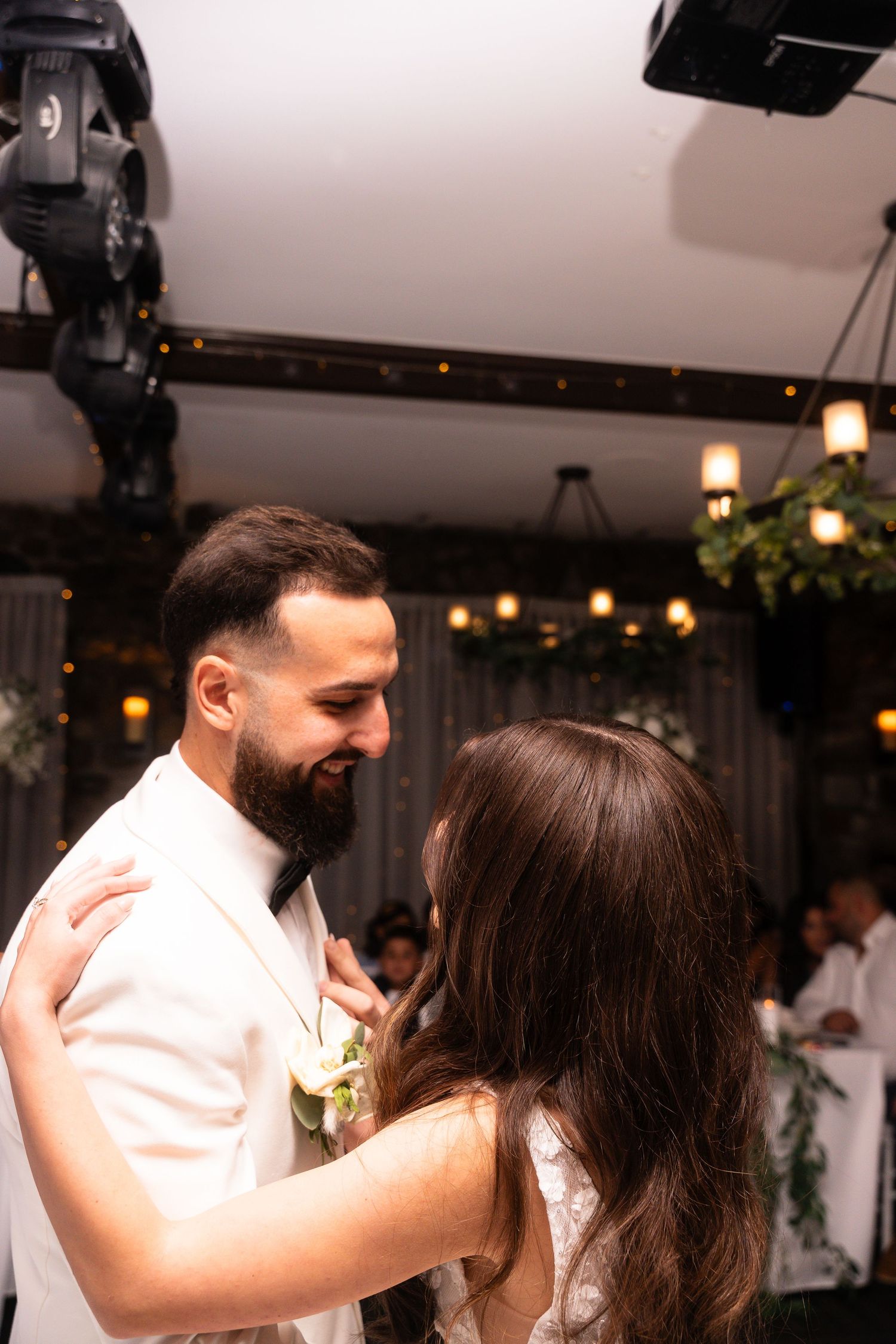 A couple shares an intimate dance moment at their wedding reception under warm lighting and greenery decor.