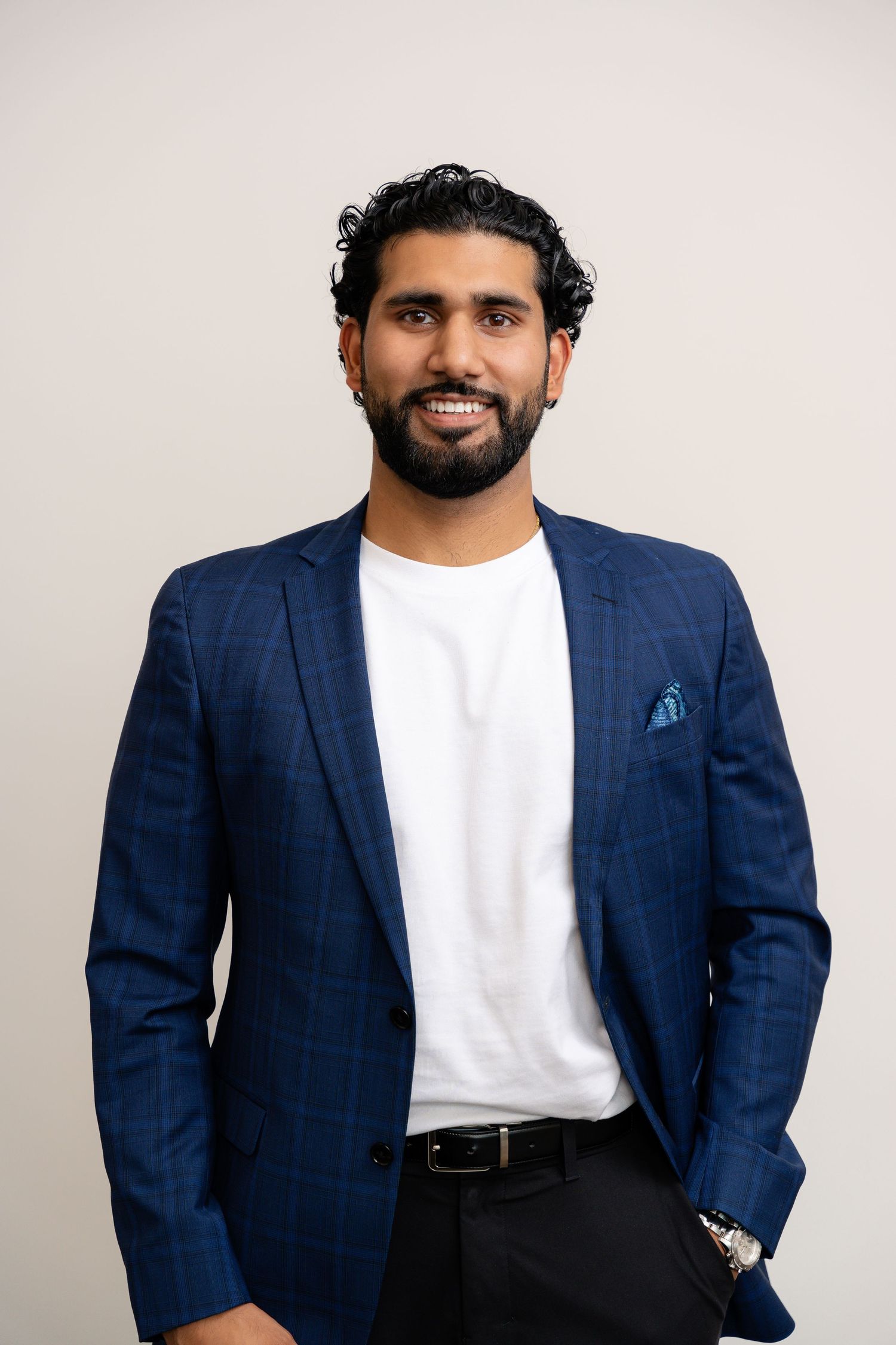 Confident professional in navy suit jacket and white t-shirt poses against neutral background.