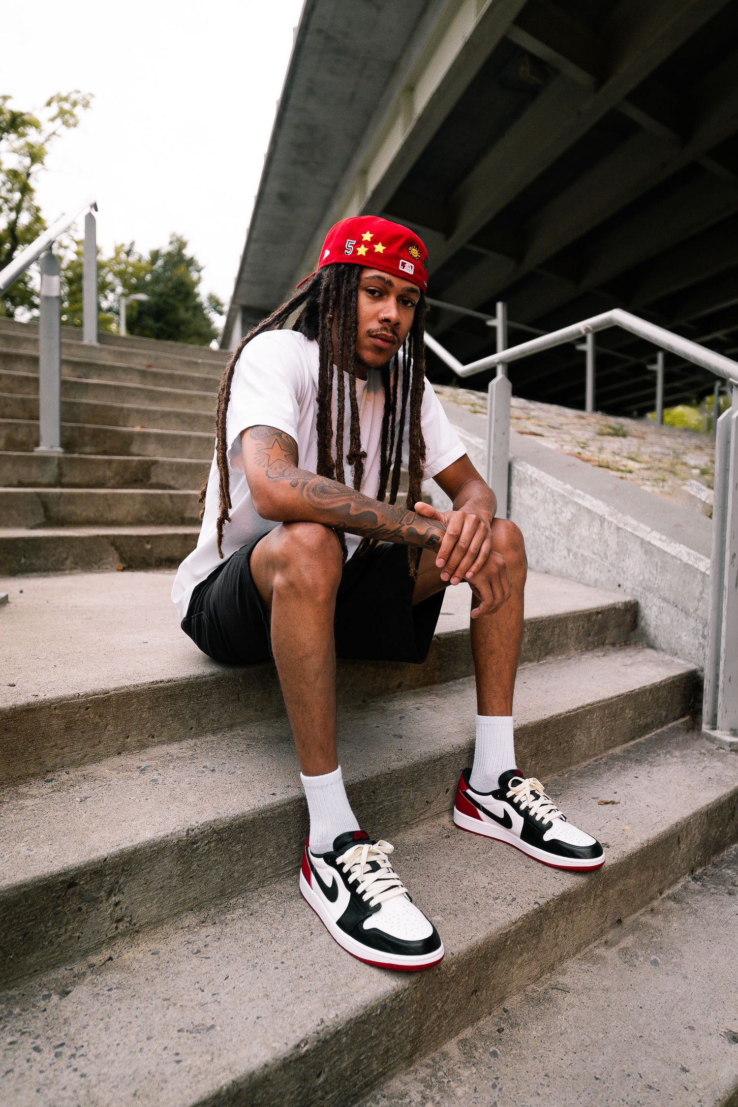 Person wearing red cap sitting on concrete steps with black and white sneakers.